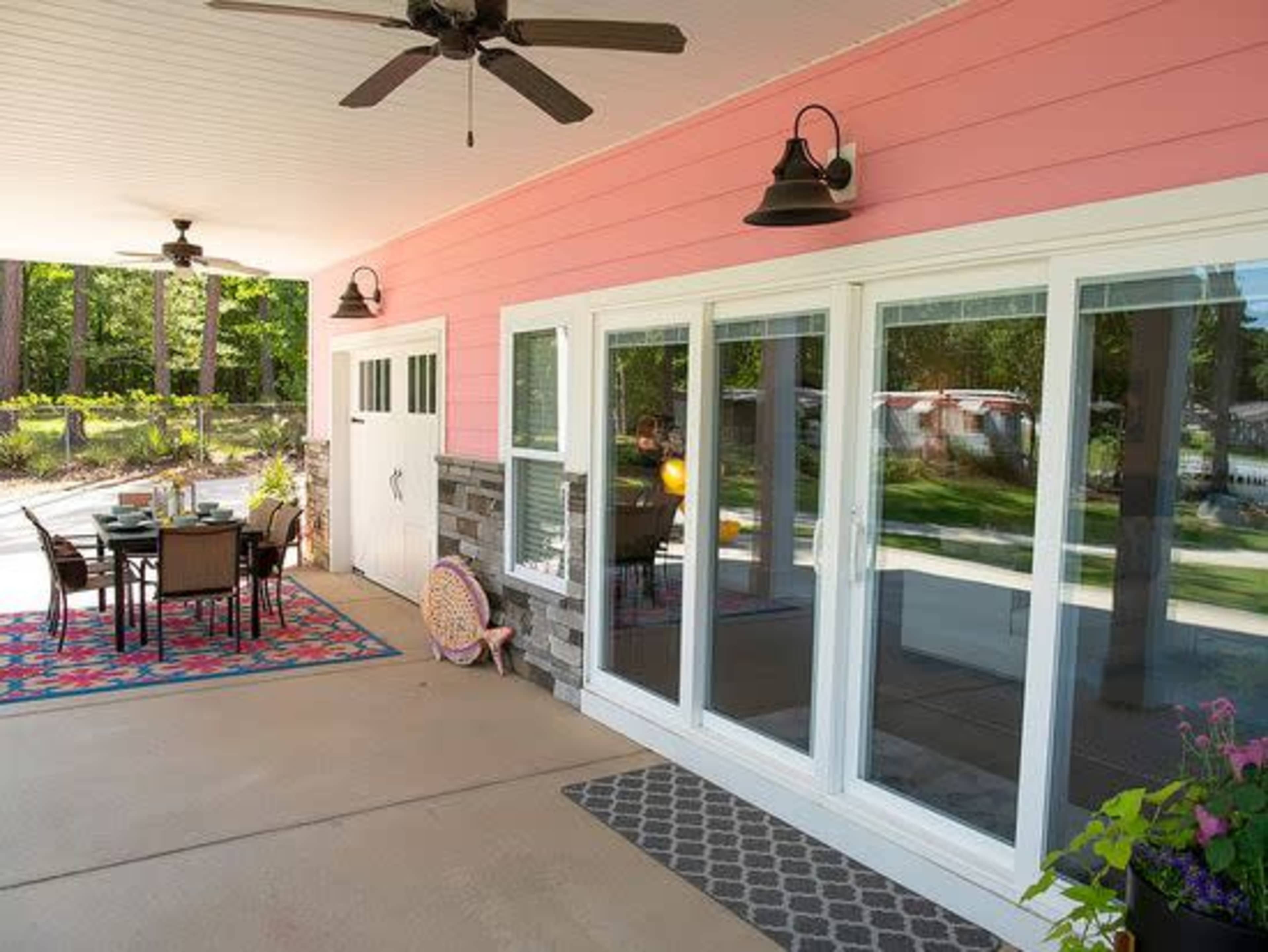 A patio area featuring a pink exterior wall, sliding glass doors, and a dining set with a table and chairs arranged on a patterned rug.