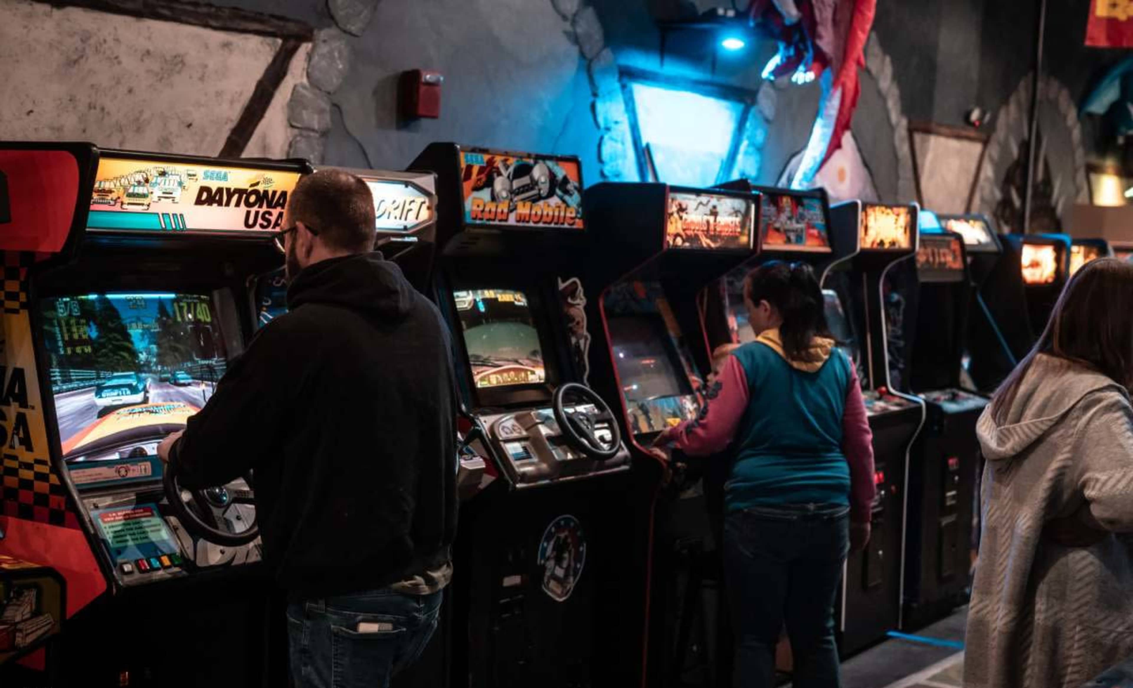 Several people are playing vintage arcade games in a dimly lit arcade setting.