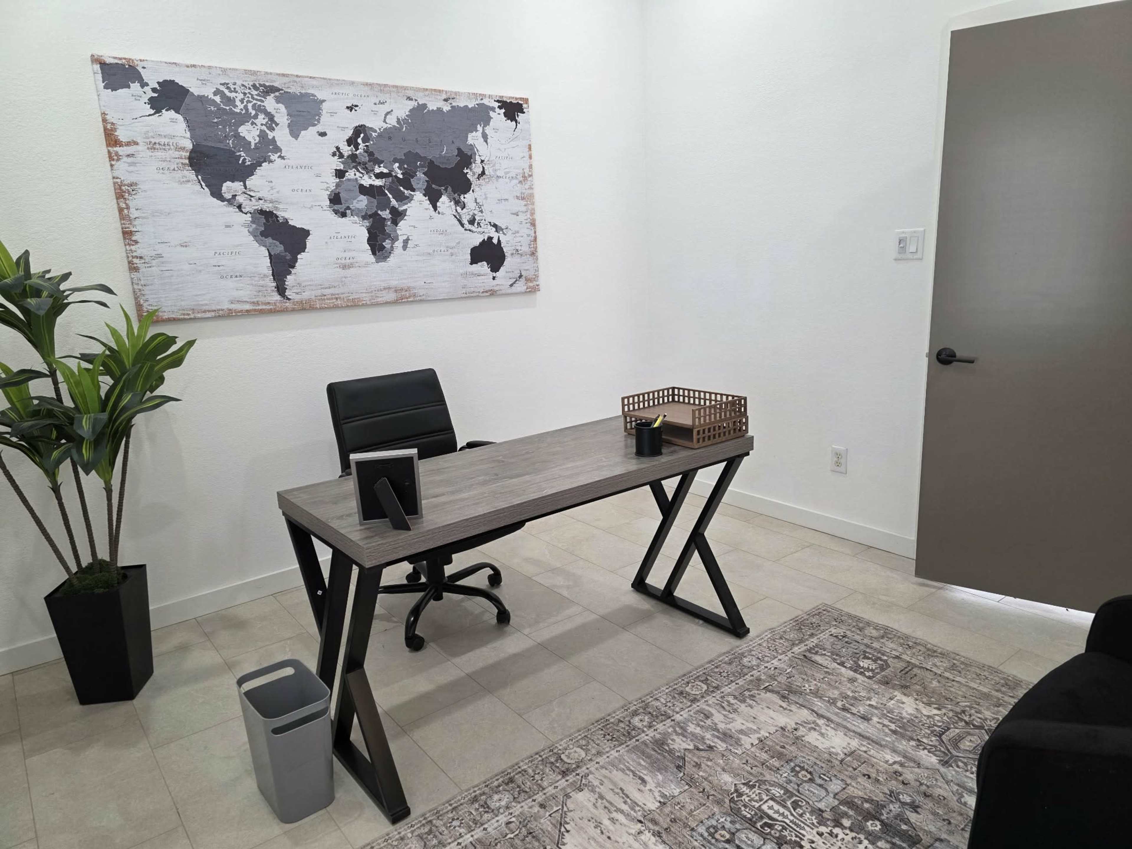 The image shows a modern office space with a map on the wall, a desk and chair, a plant, and a wastebasket.