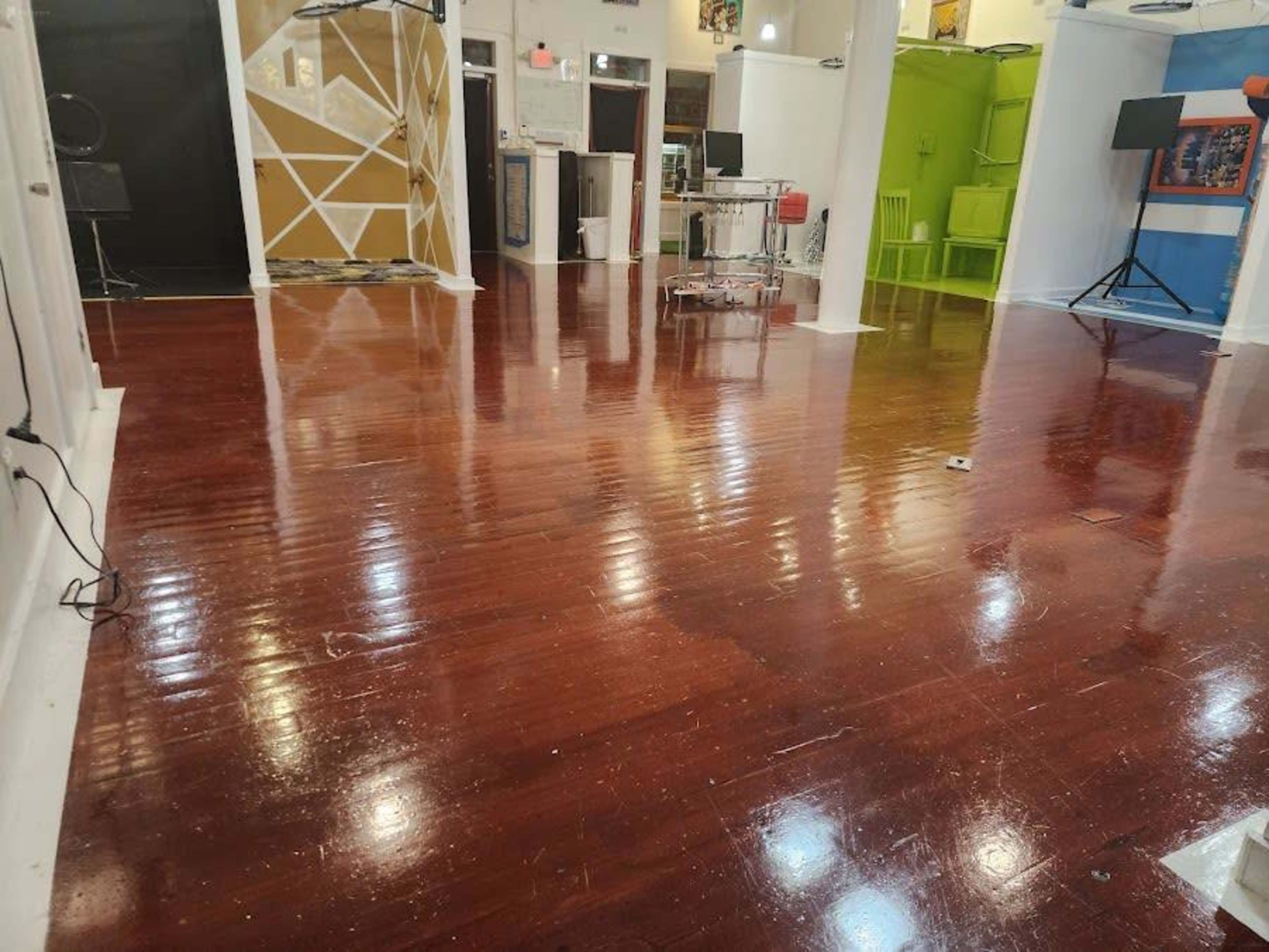 A spacious room with polished wooden flooring and various brightly colored walls in the background.