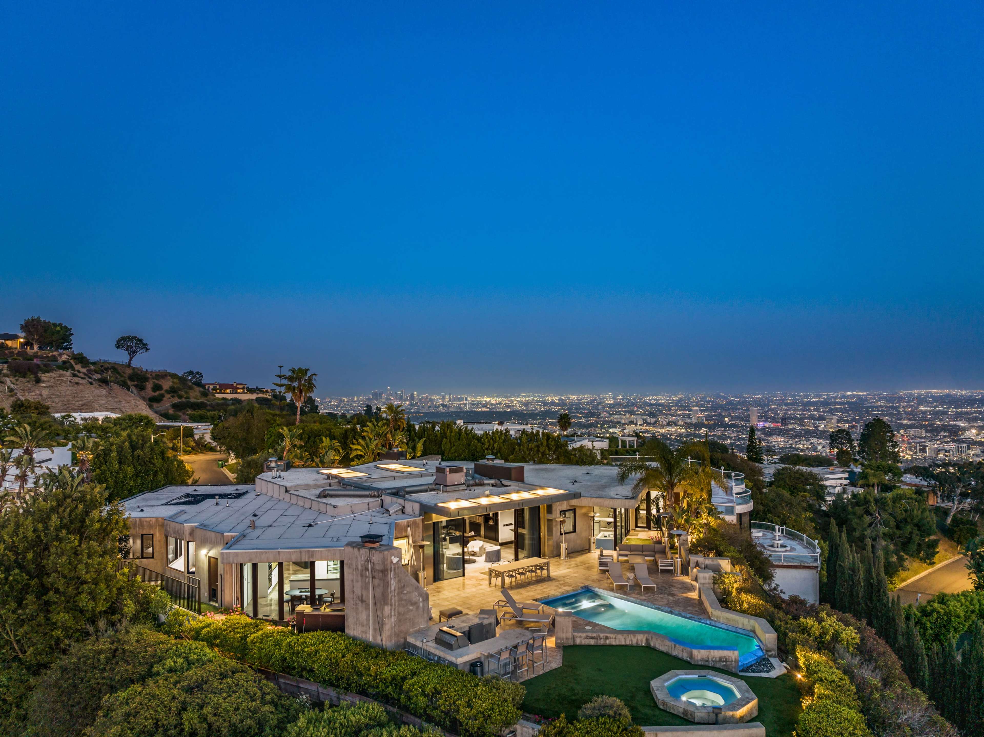 A modern hillside house with a pool and spa, overlooking a cityscape at twilight.