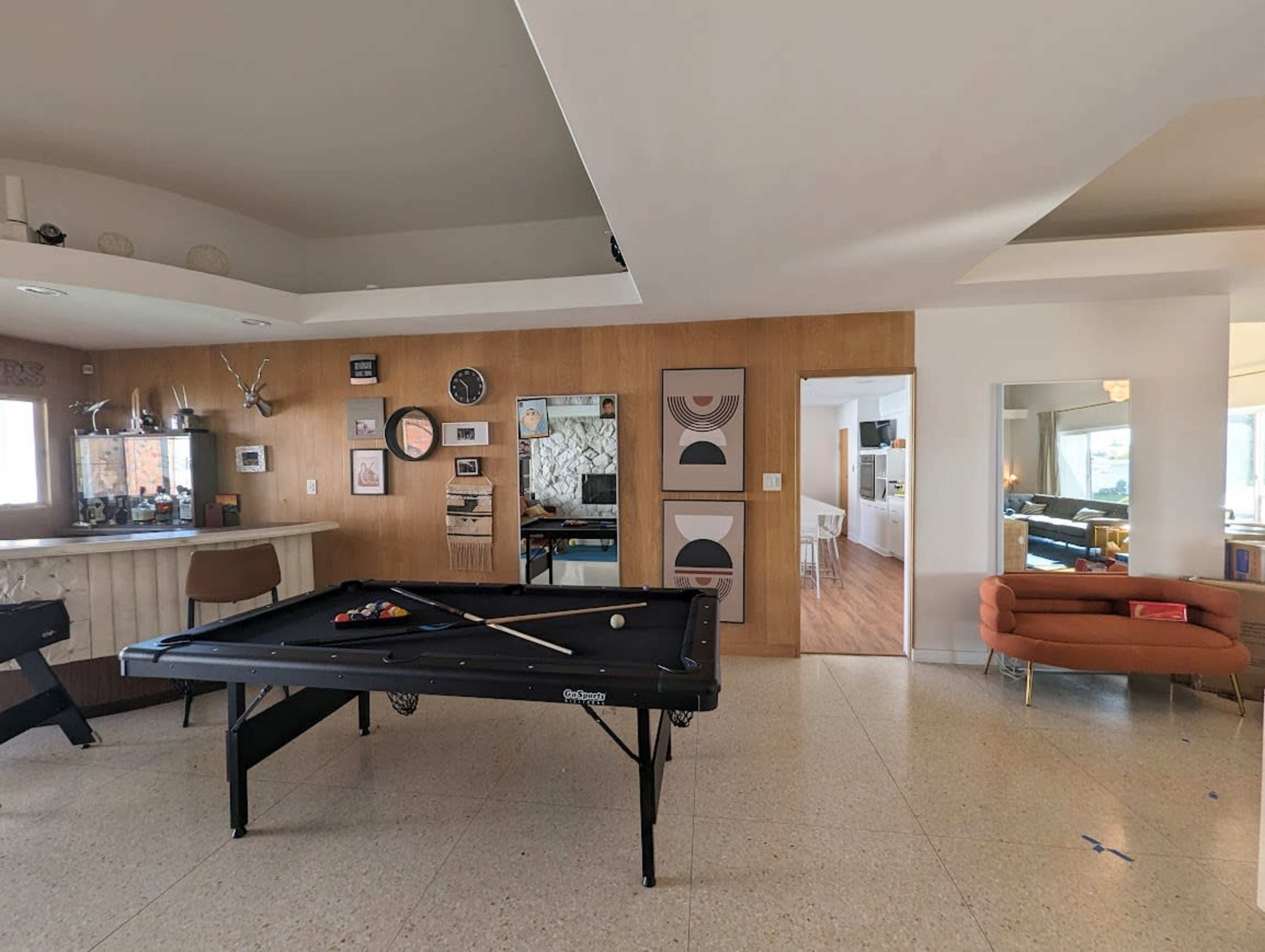 A spacious living area featuring a billiard table in the foreground, with a wooden accent wall and various decorations in the background.