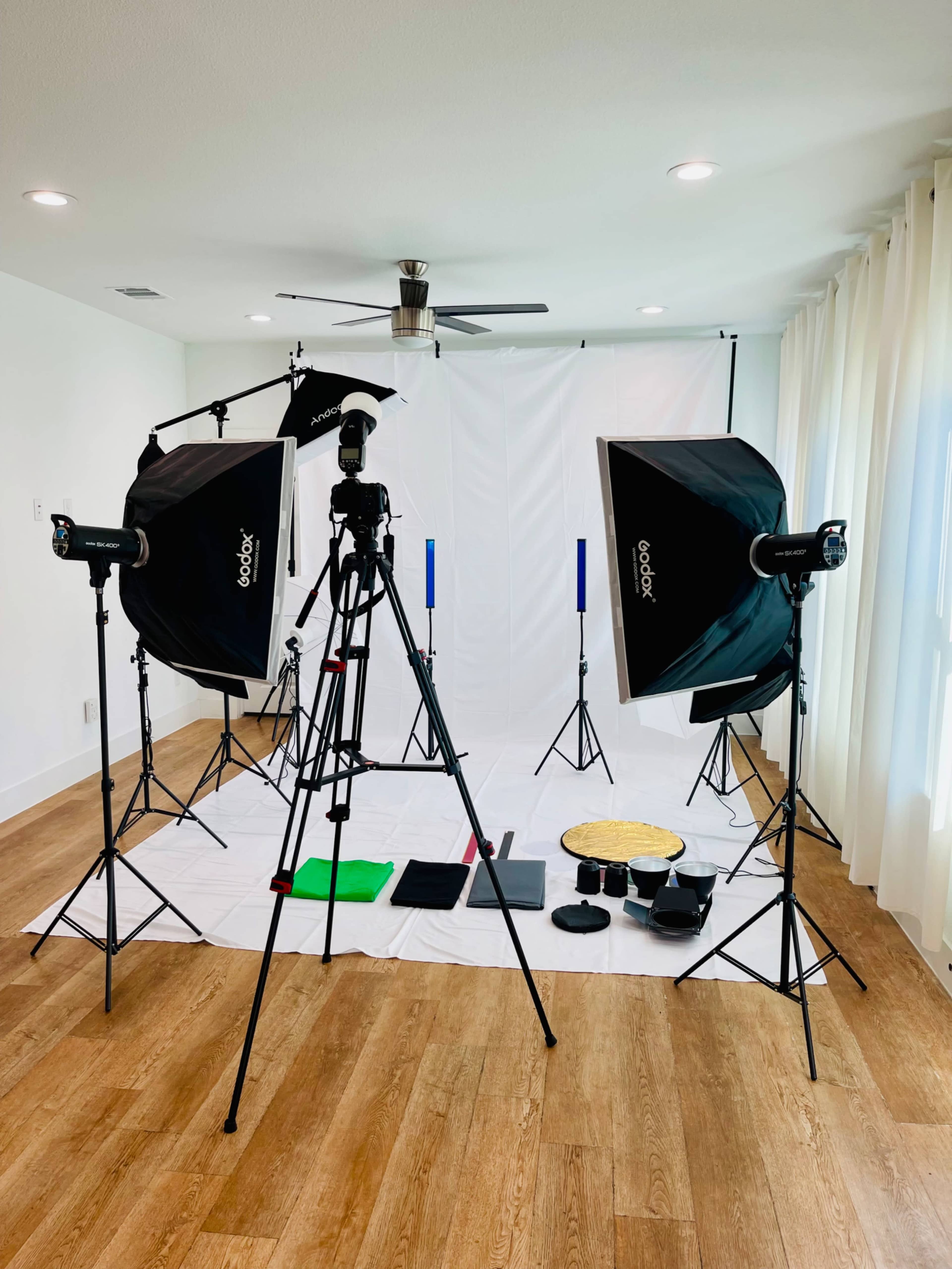 A photography setup featuring a camera on a tripod surrounded by softbox lighting and various props arranged on a white backdrop in a well-lit room.