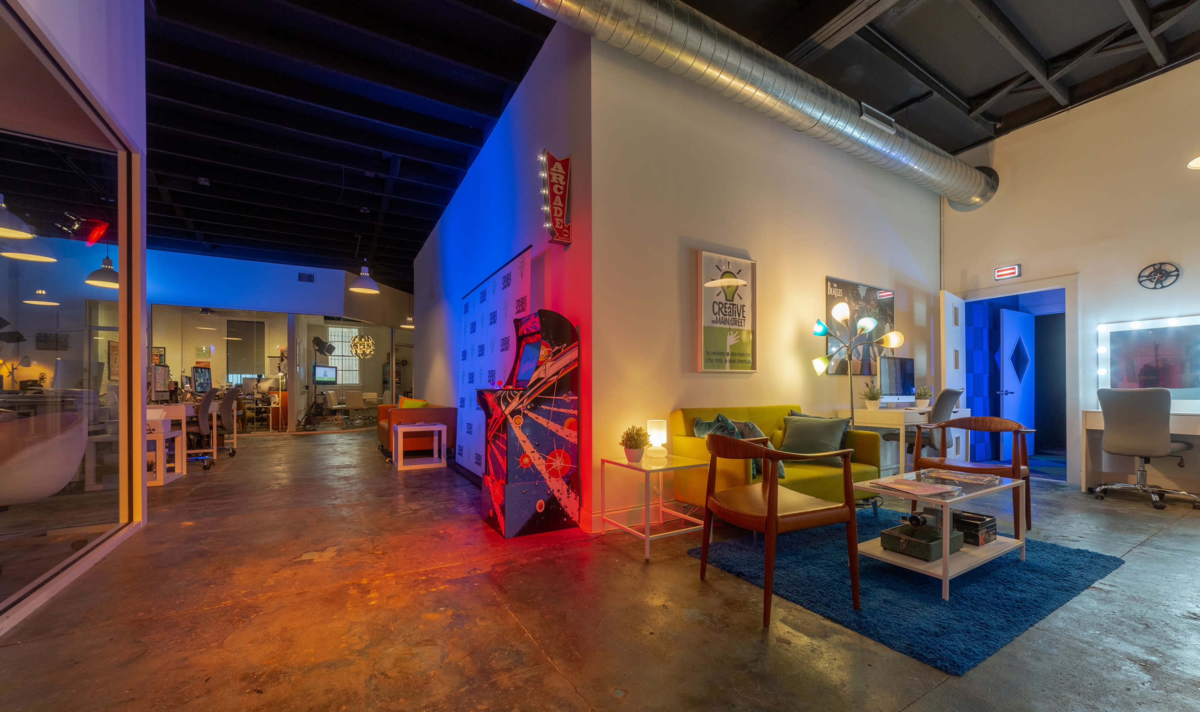 A modern office space with a lounge area featuring comfortable seating, vibrant lighting, and an arcade machine.