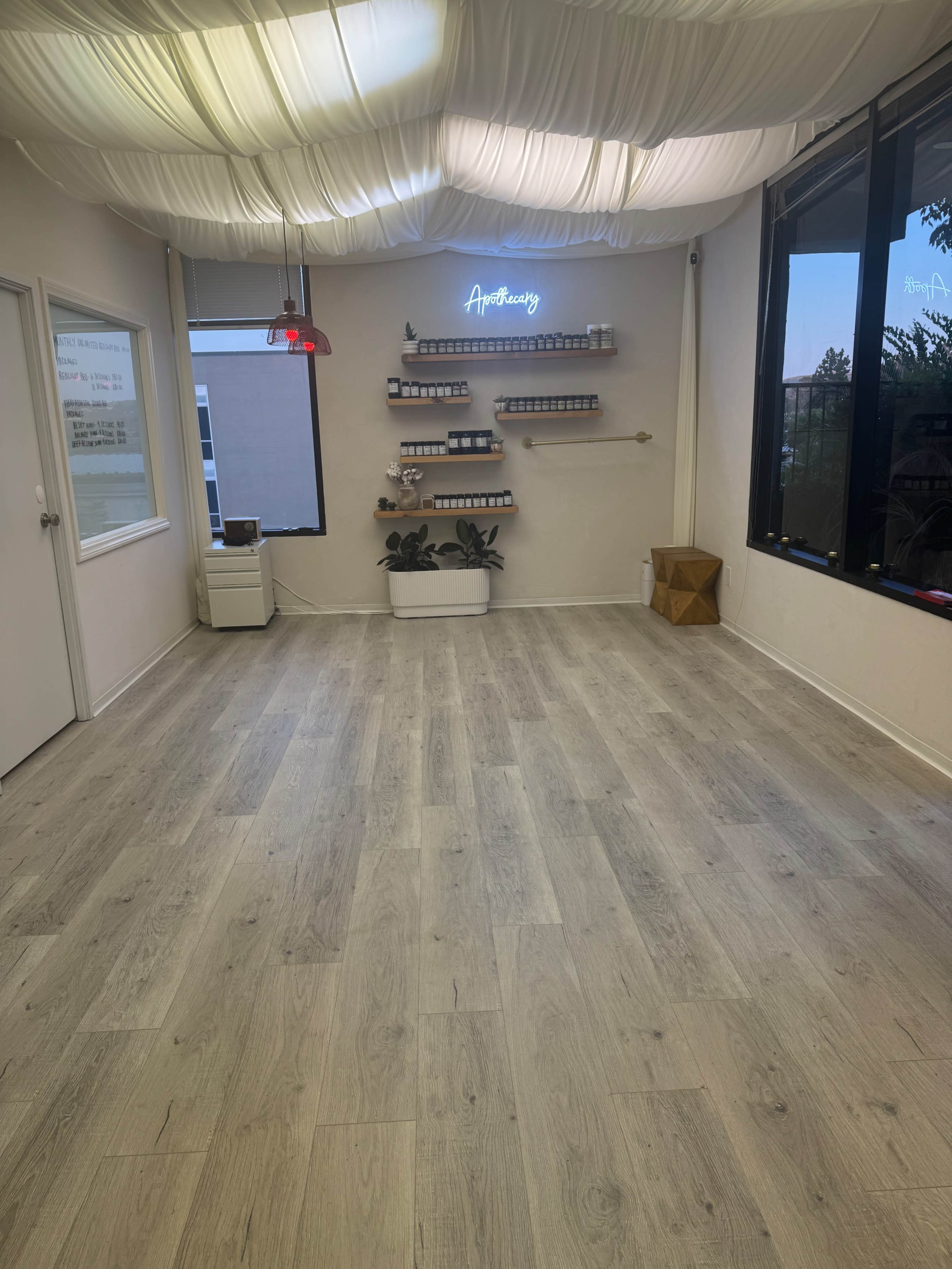 The image shows a vacant, well-lit room with light-colored wooden flooring and a decorative wall shelf displaying various products.