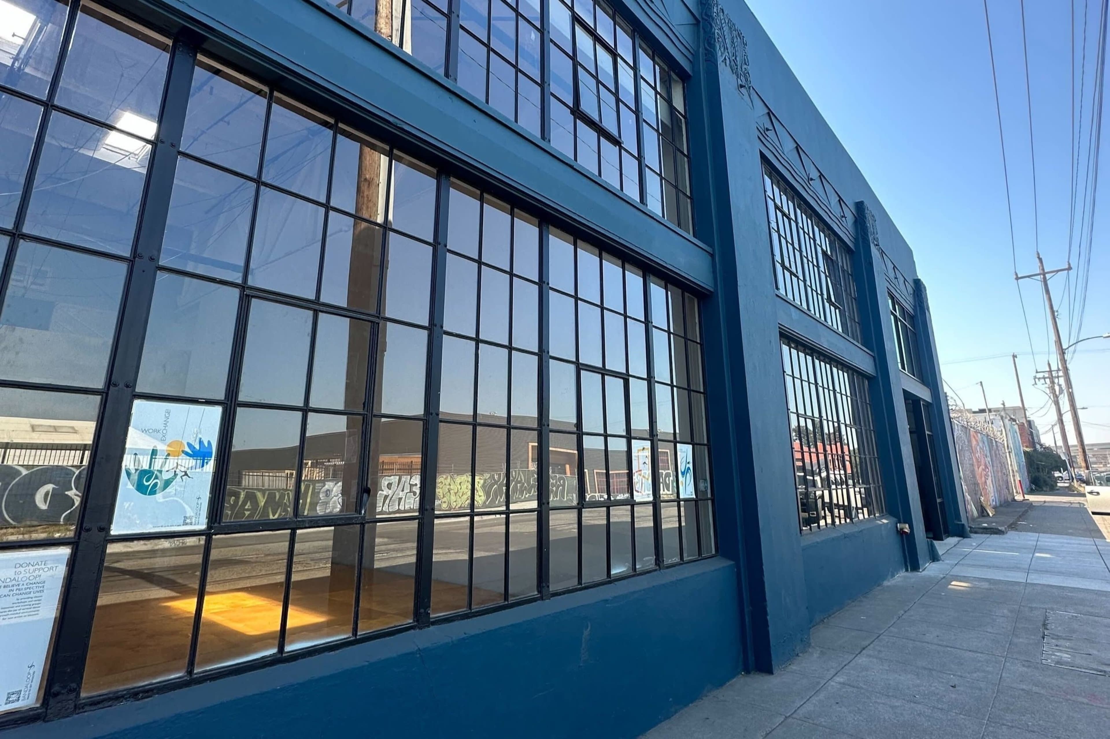 The image shows a blue building with large windows reflecting the clear sky and street scenery.