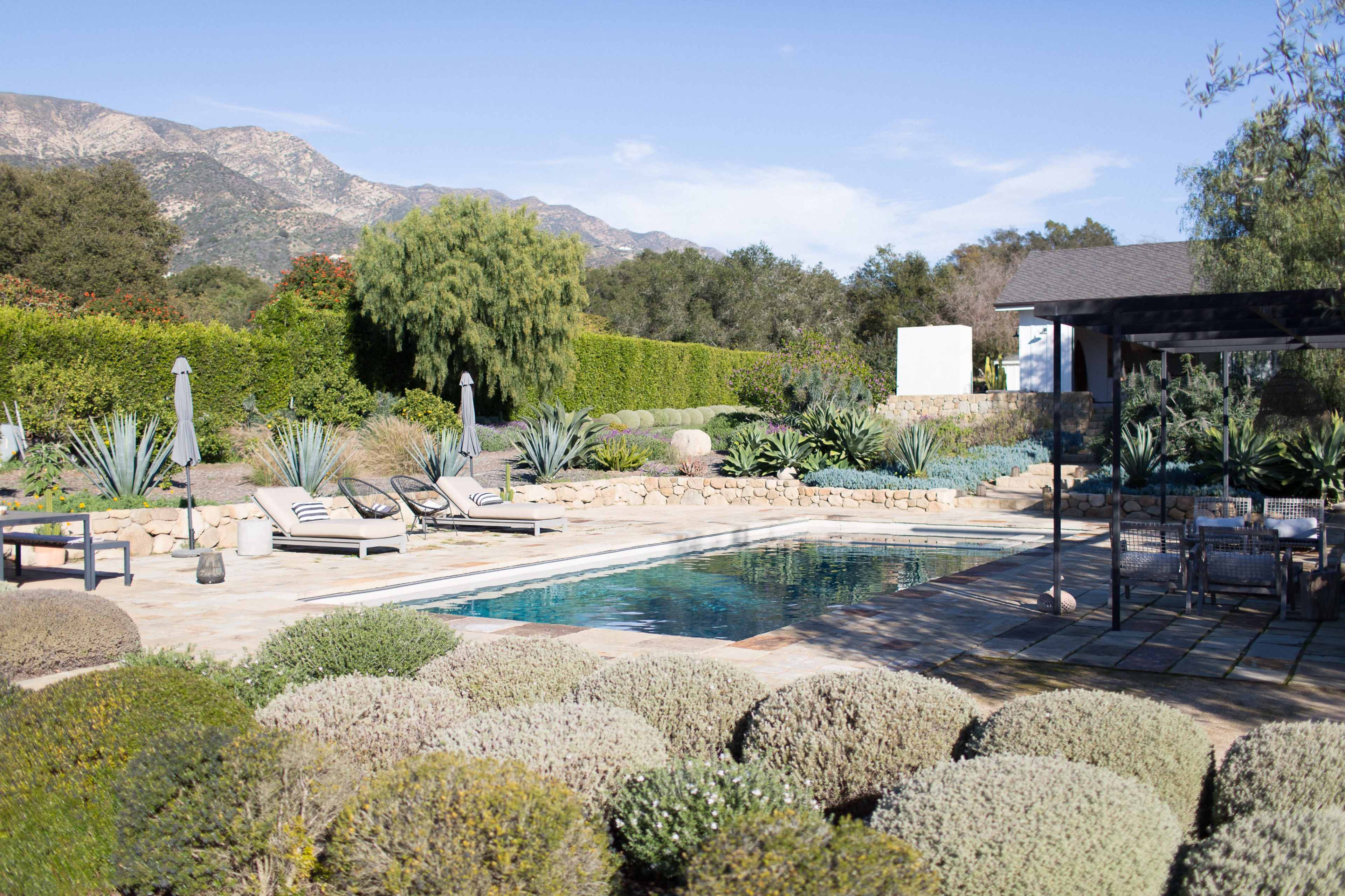 A swimming pool is surrounded by landscaped gardens, loungers, and mountains in the background.