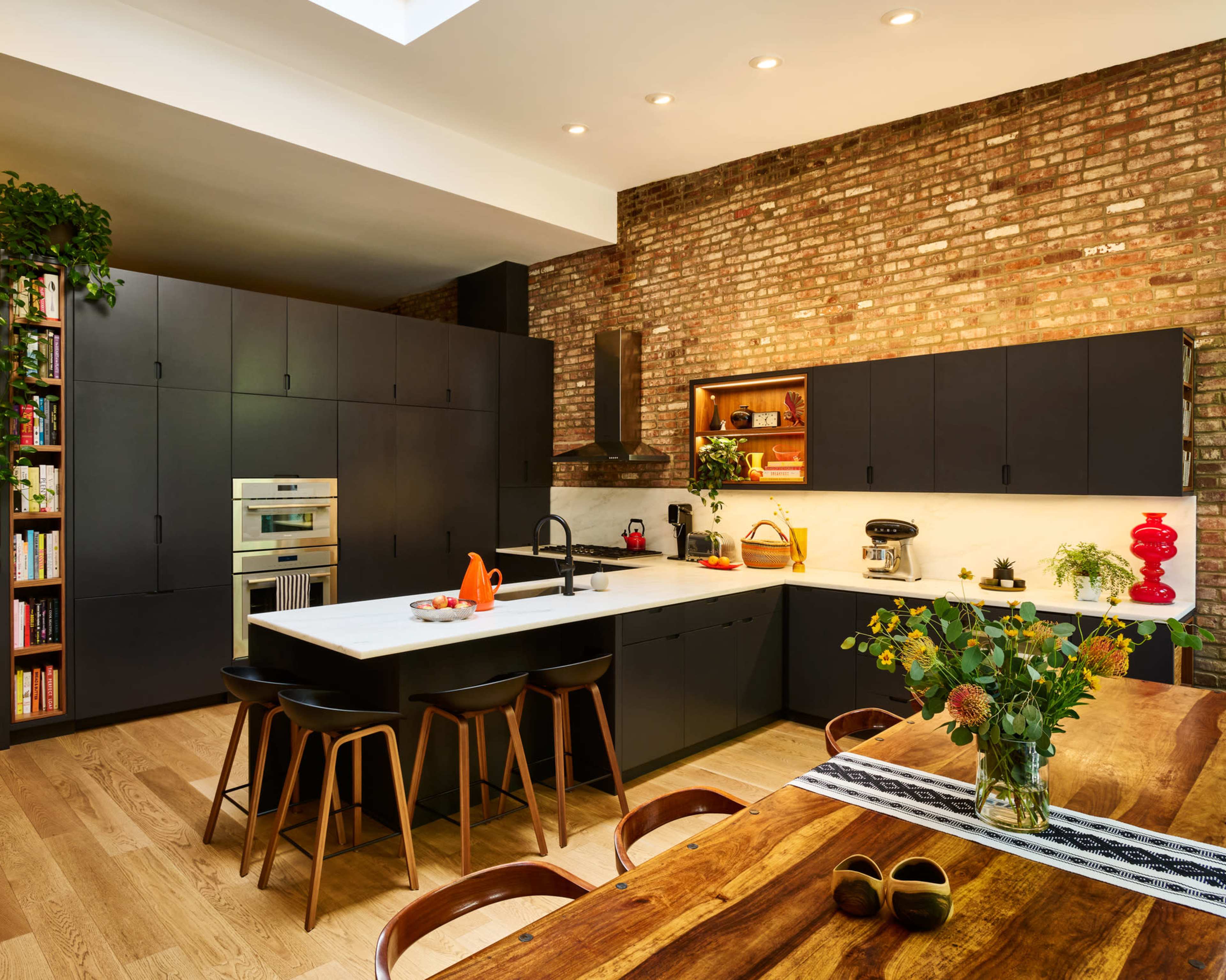 The image shows a modern kitchen with dark cabinetry, a spacious island, and a wooden dining table adorned with a vase of flowers.