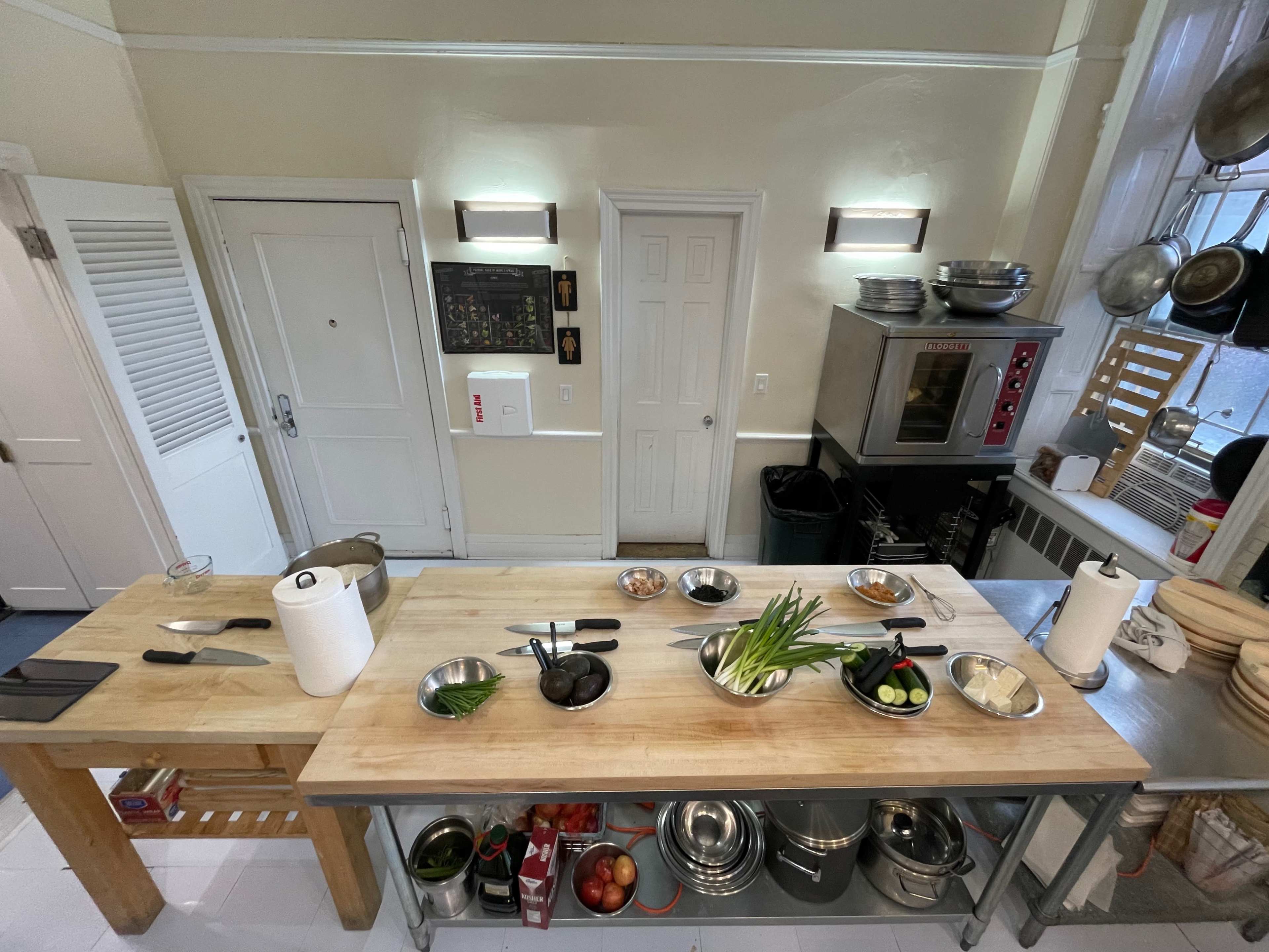 A kitchen with a wooden prep table, various bowls of ingredients, an oven, and shelves filled with pots and utensils.