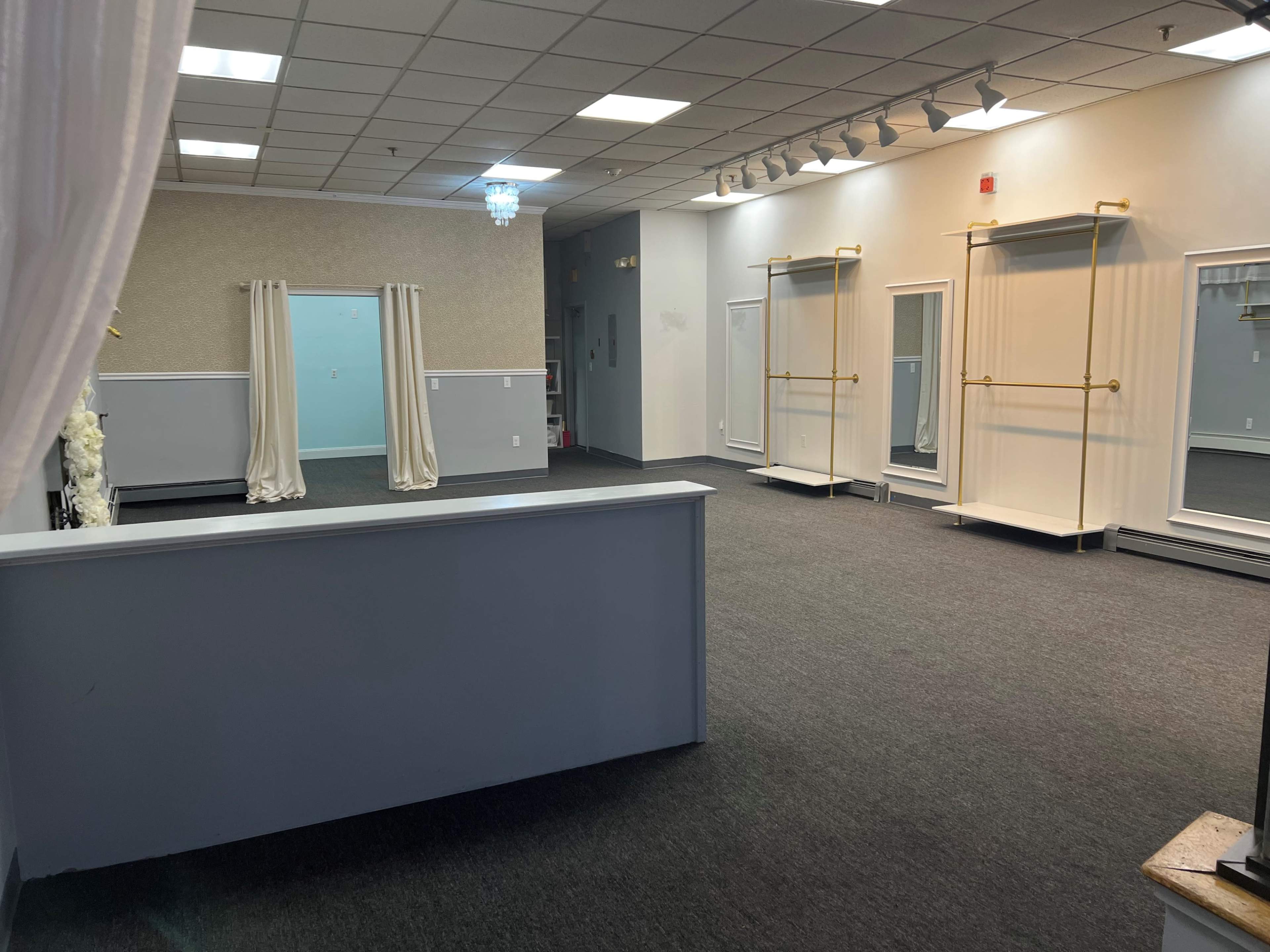 A spacious interior of a retail or showroom area with gray carpeting, several mirrors mounted on the walls, and a reception counter in the foreground.