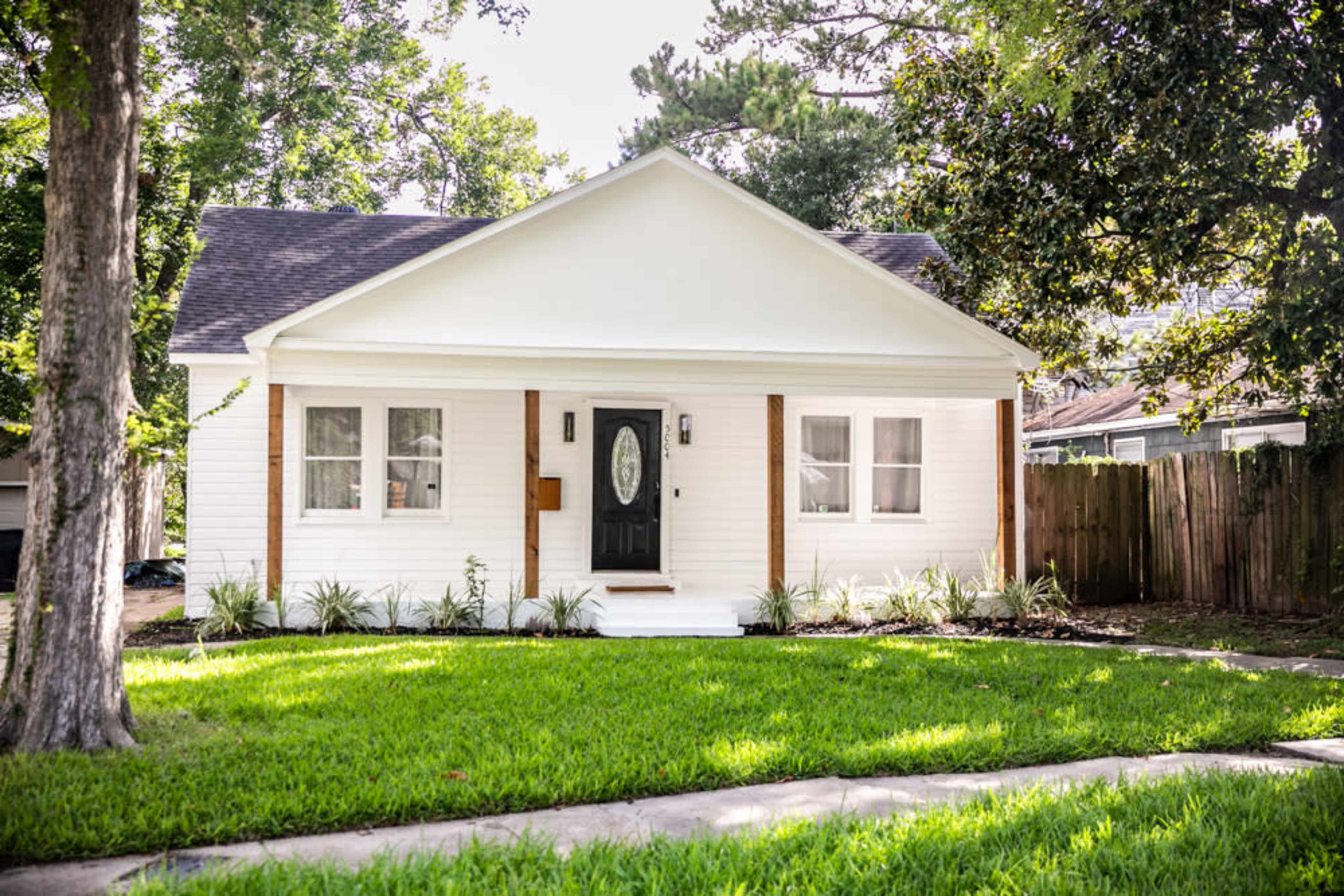 A single-story white house with a black front door is surrounded by a green lawn and trees.