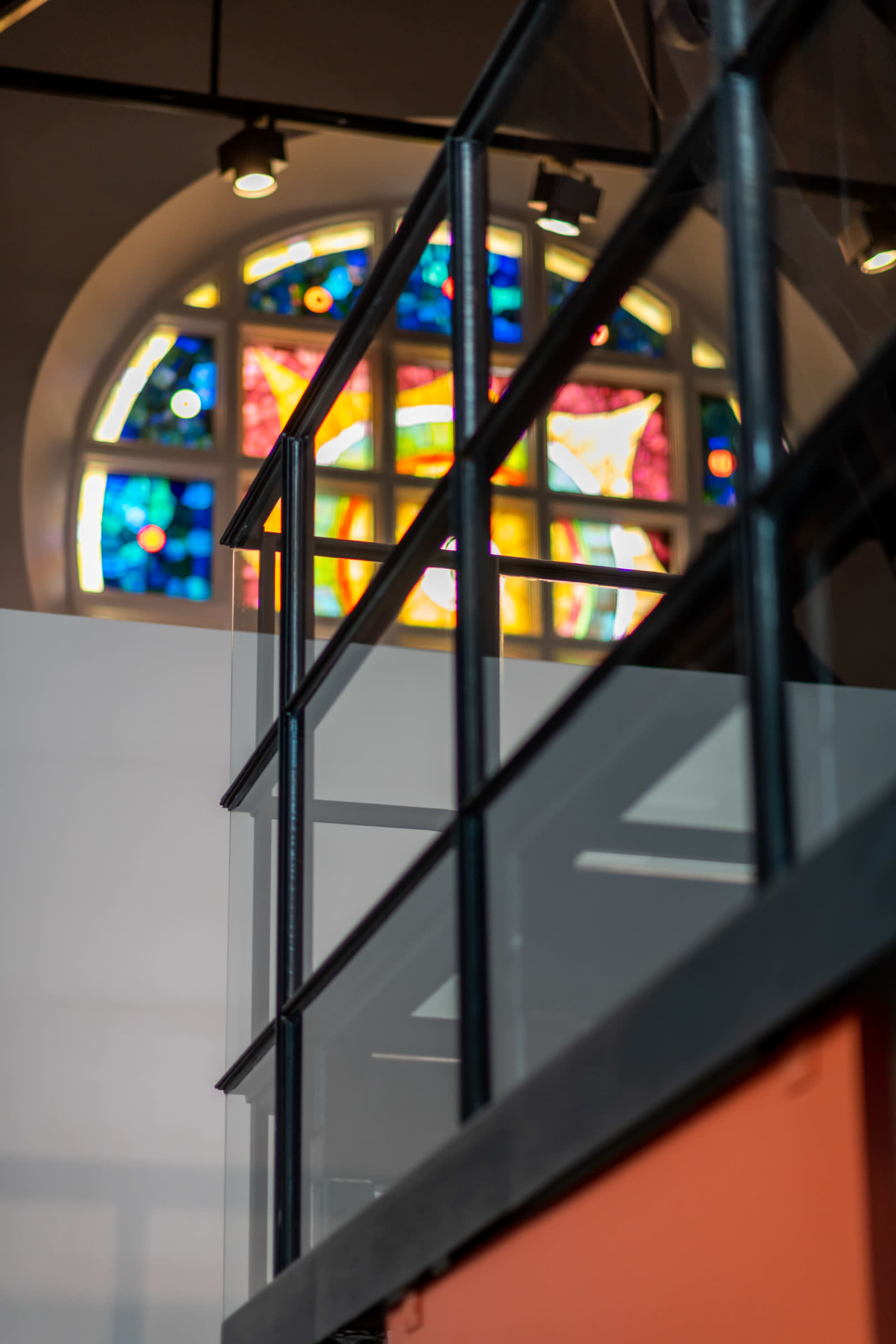 A modern staircase railing leading up to a brightly colored stained glass window.