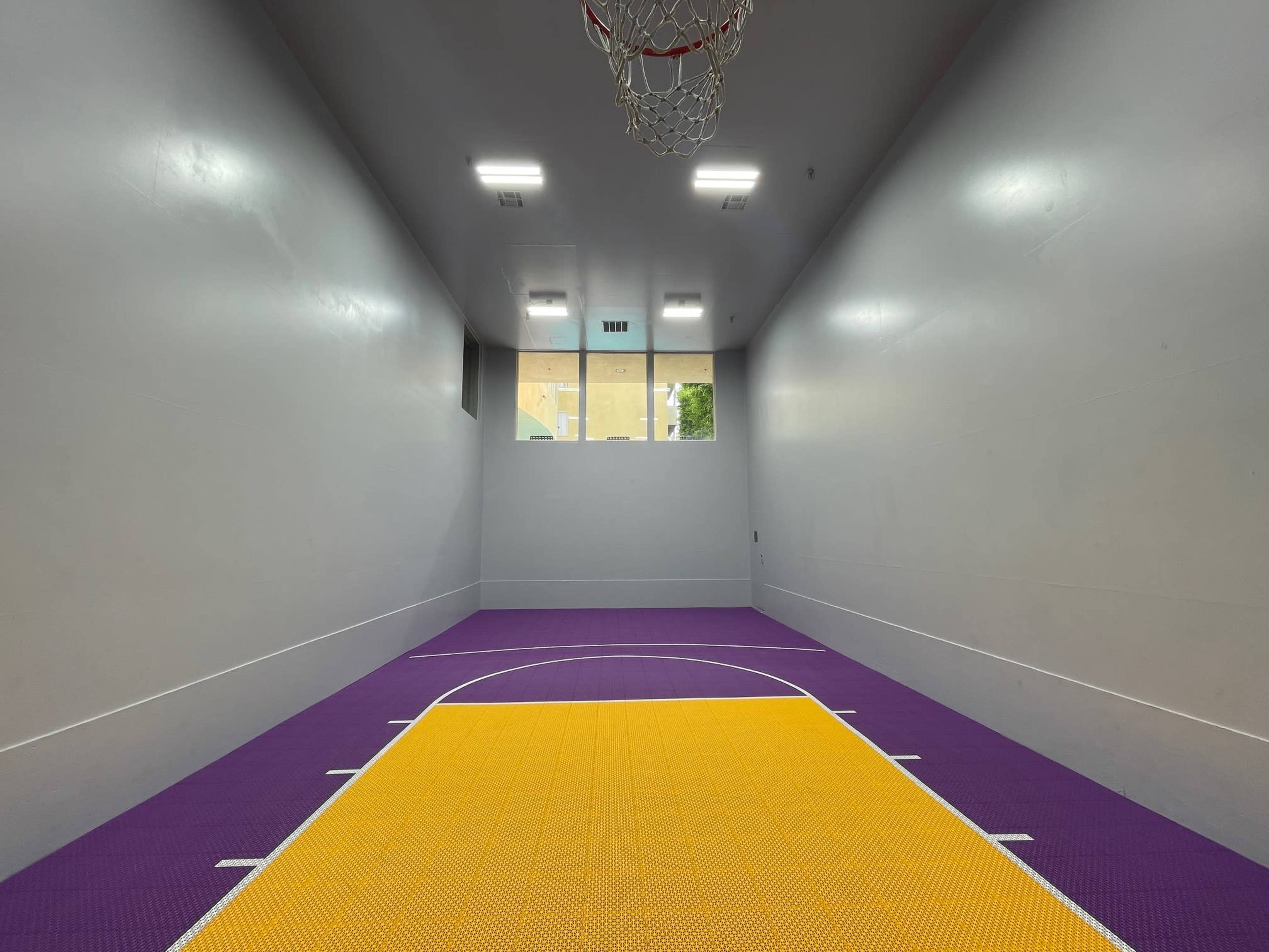A small indoor basketball court with a purple and yellow floor and a single basketball hoop mounted on the wall.