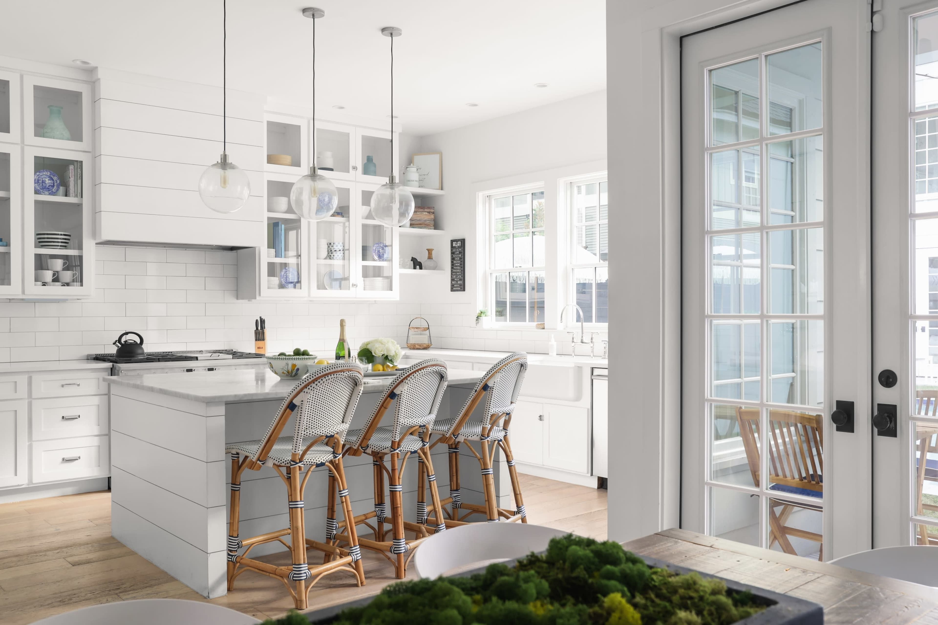 A modern kitchen features white cabinetry, a large island with bar stools, and a door leading to an outdoor area.