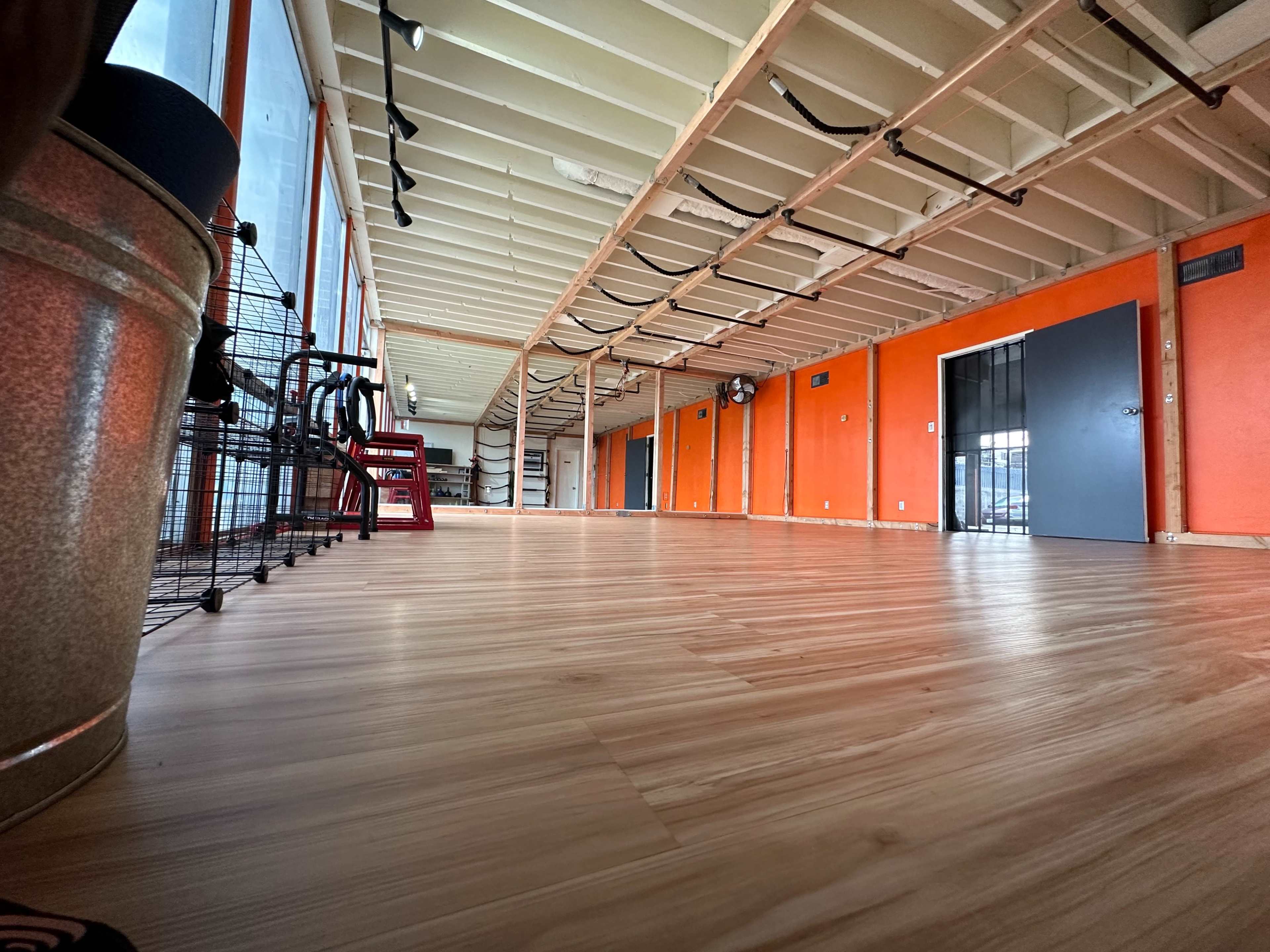 A spacious, empty room with wooden flooring, orange-painted walls, and exercise equipment along one side.