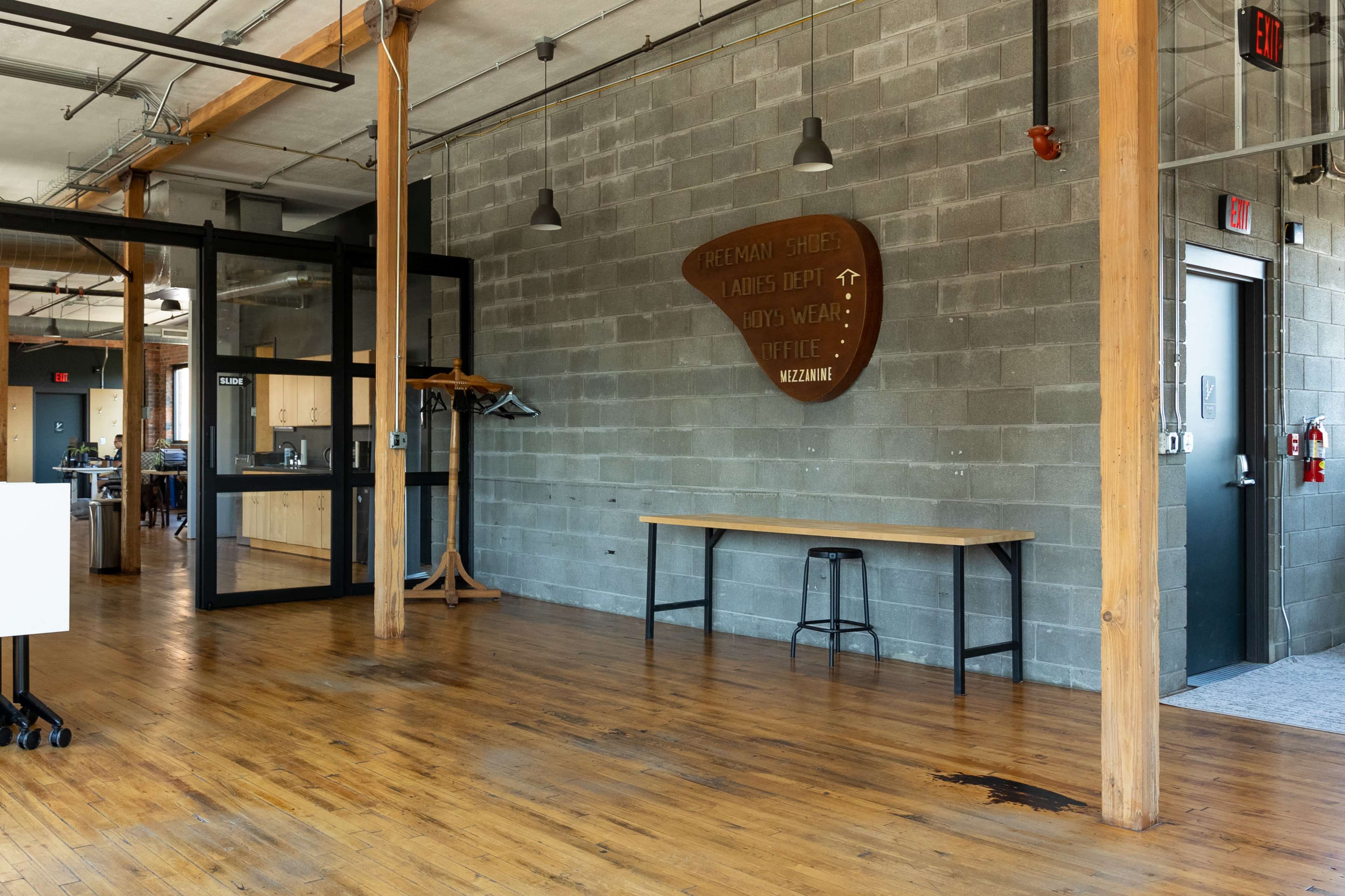 An interior workspace with wooden flooring, gray concrete walls, and a long table against the wall.