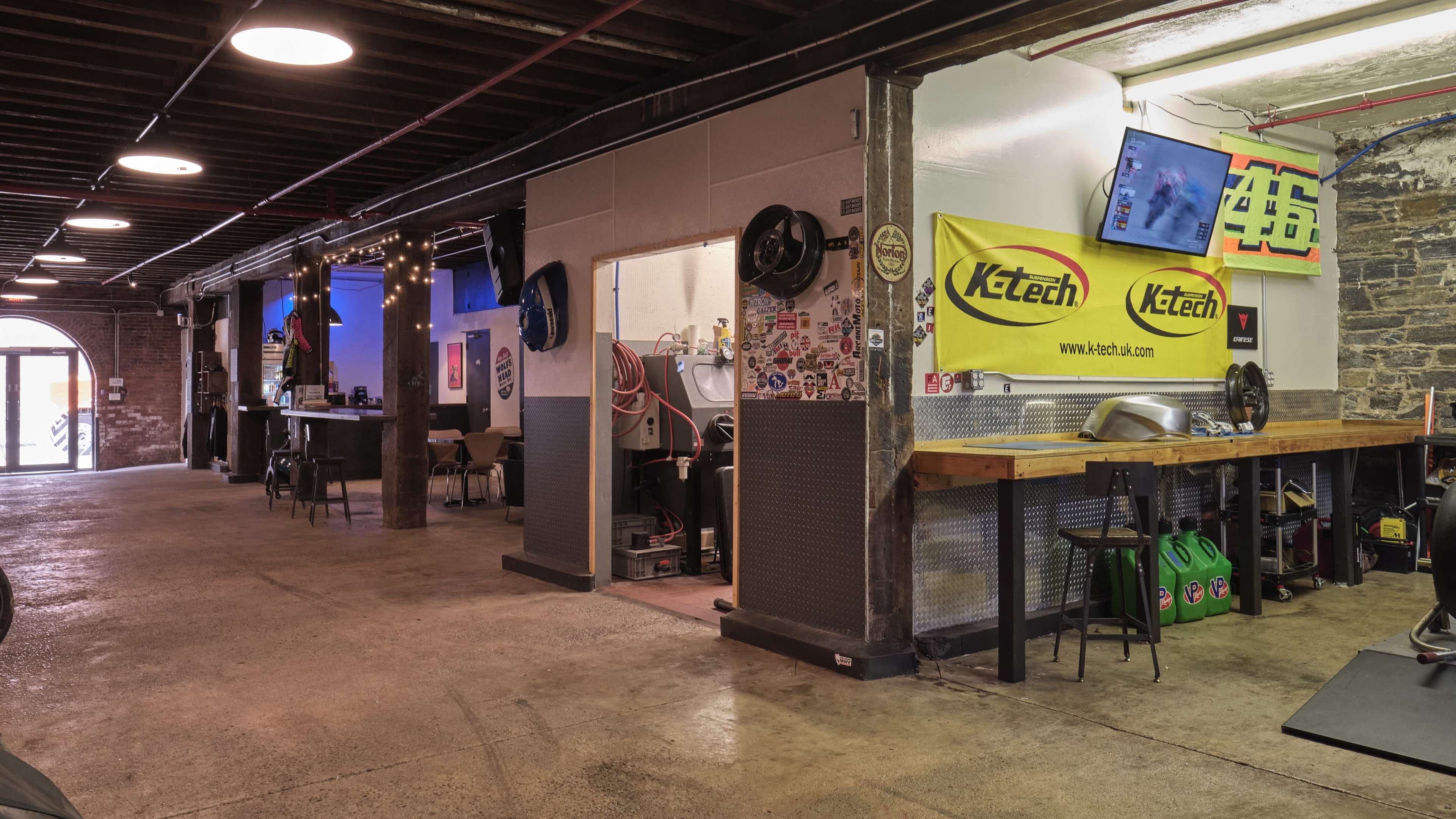 A spacious, industrial-style workshop with exposed brick walls, a counter, and various equipment, including monitors and banners.
