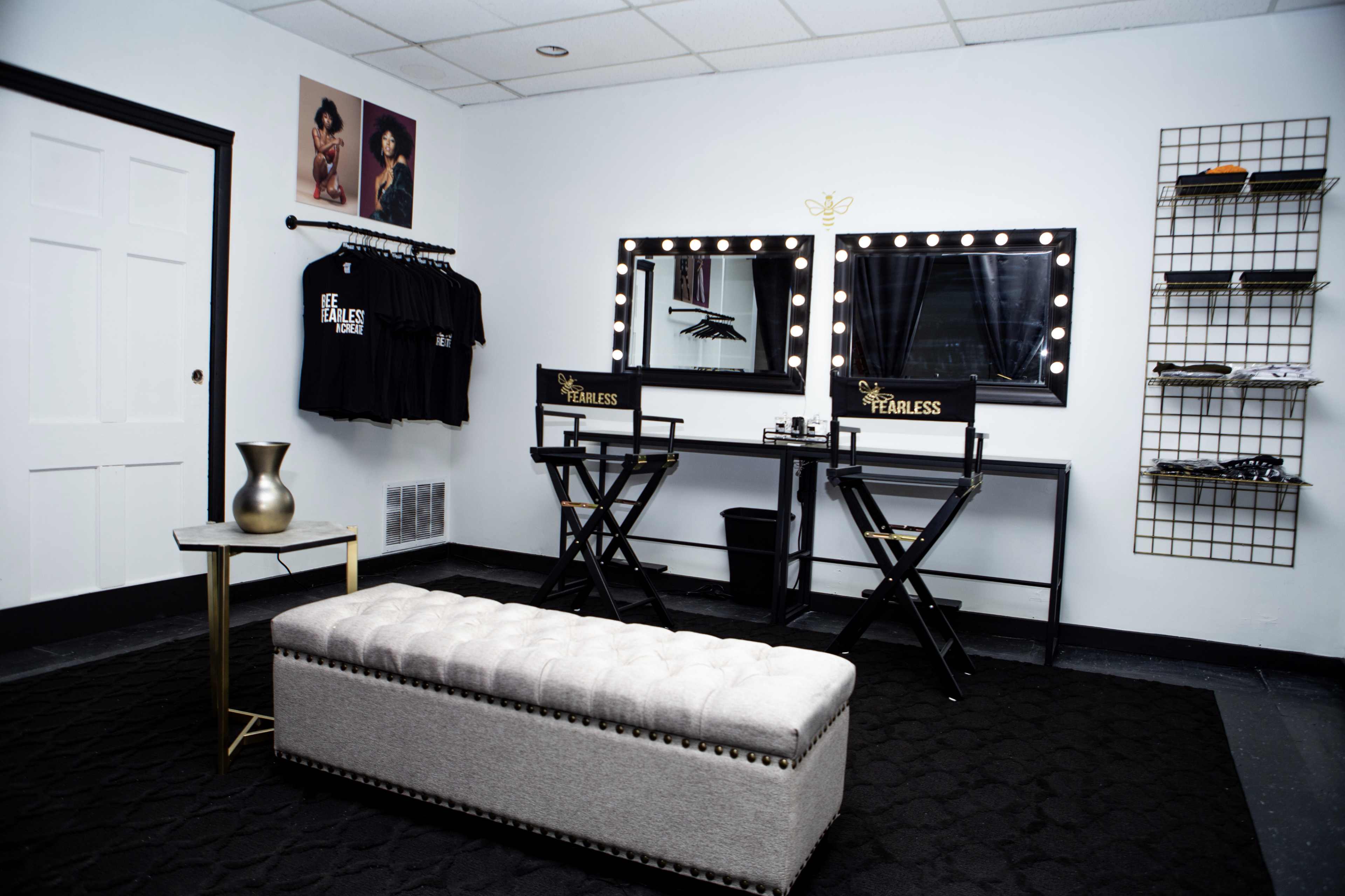 A beauty room features two mirrored makeup stations with director's chairs, a tufted bench, and a decorative wall display of products.