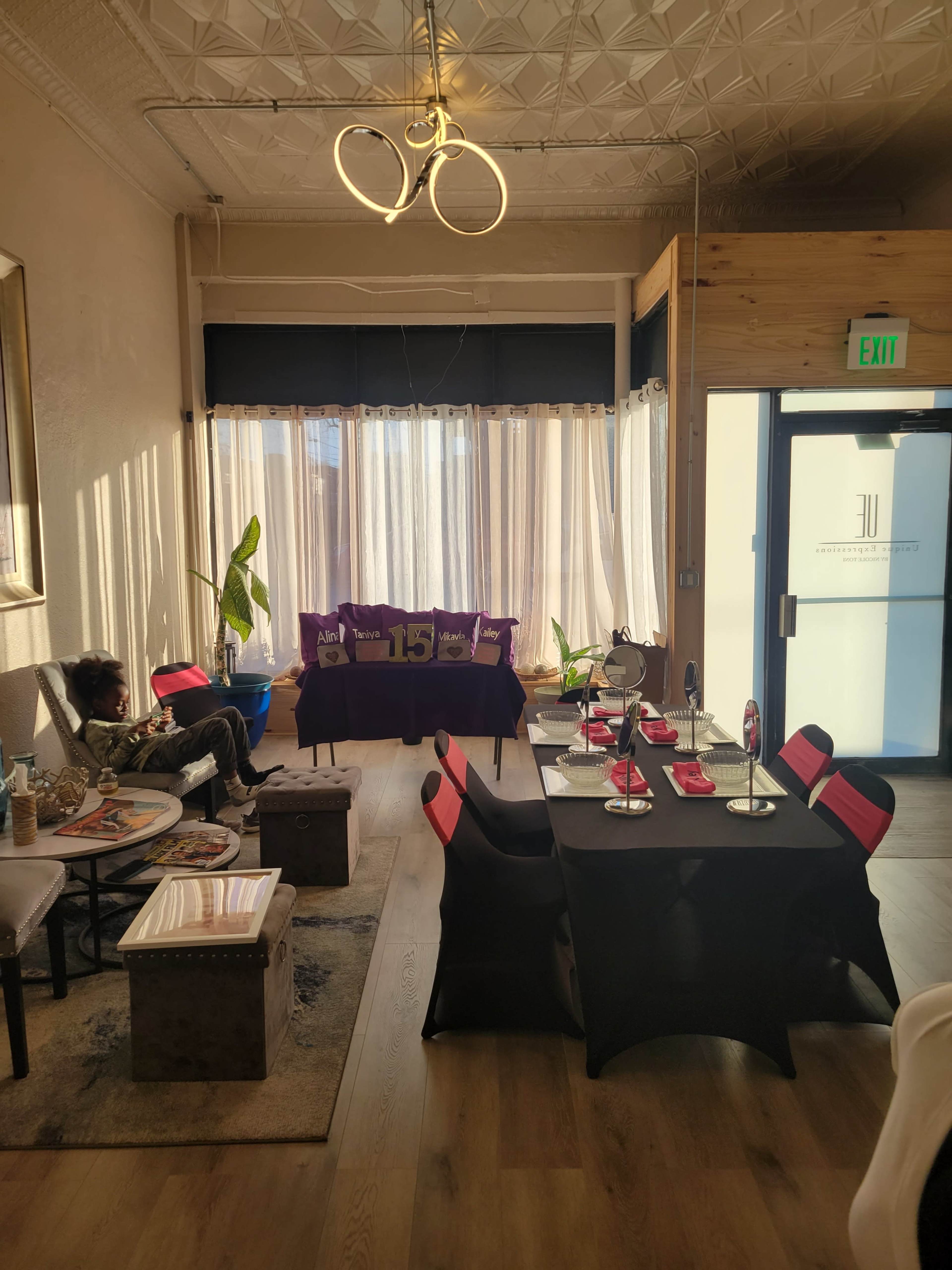 The image shows a modern, indoor space with a seating area featuring a couch, plants, and a dining table set for an event.