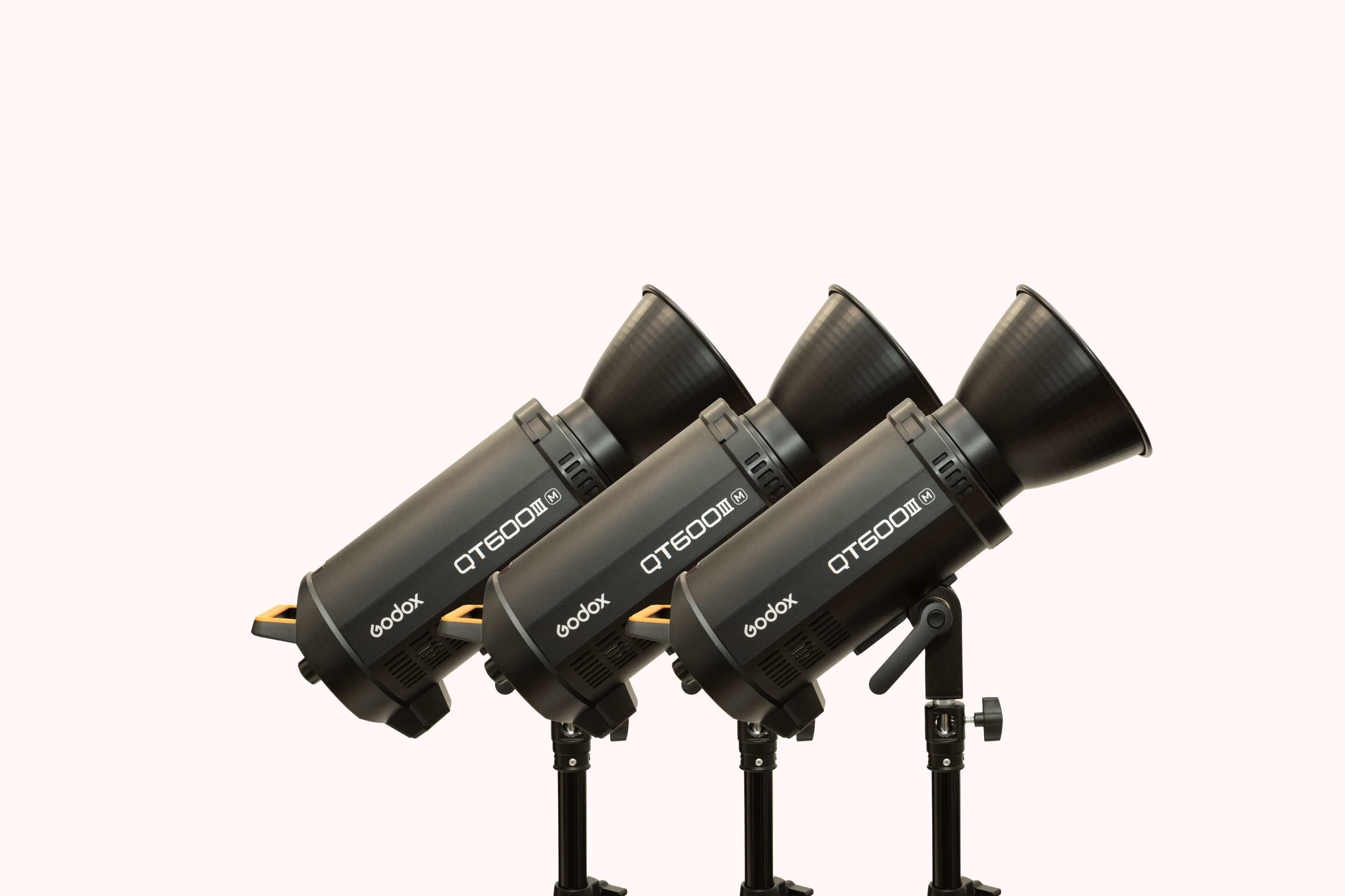 Three studio lights are arranged in a row on black stands against a neutral background.