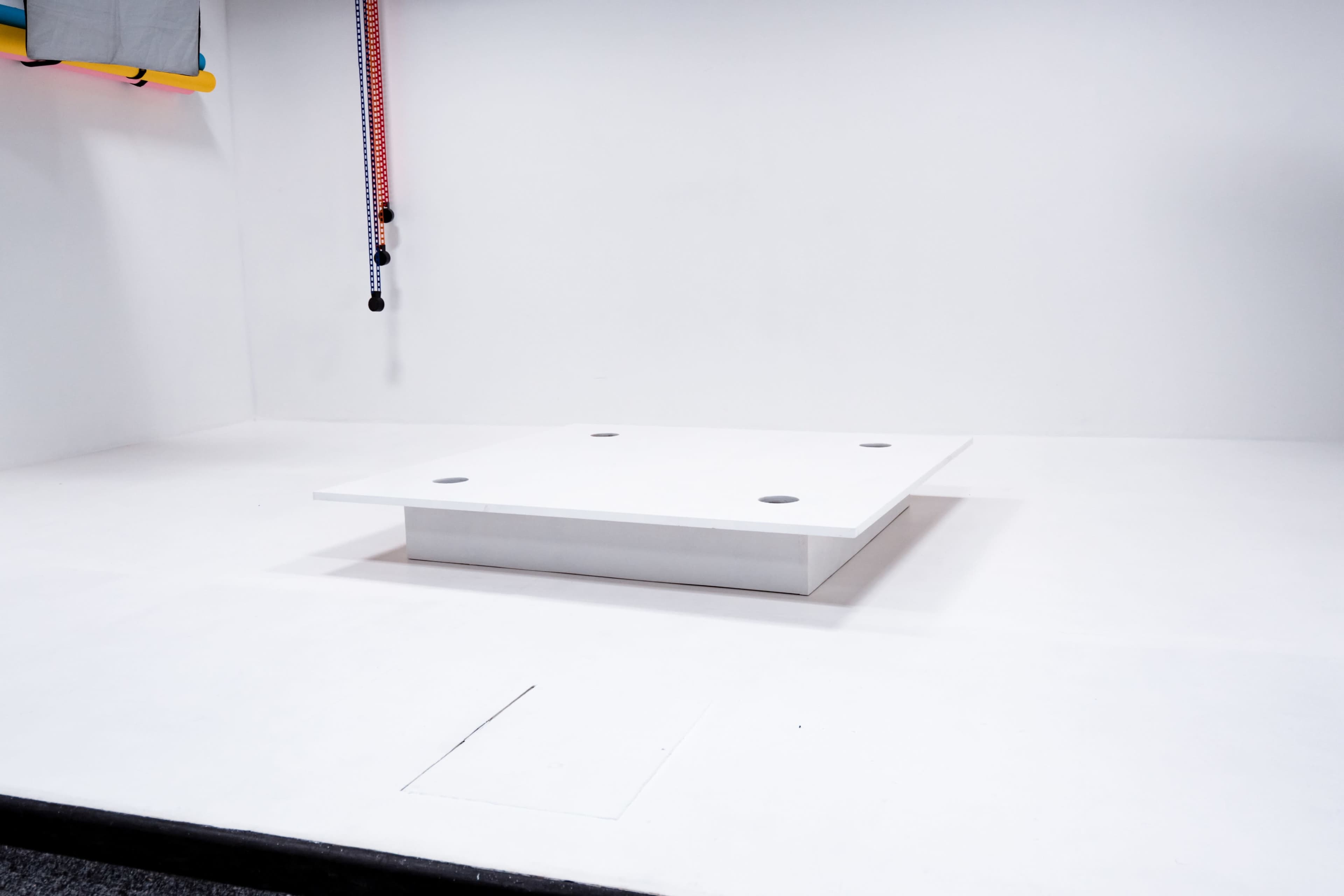 A rectangular white platform with four circular cutouts sits in the center of a minimalist white room.