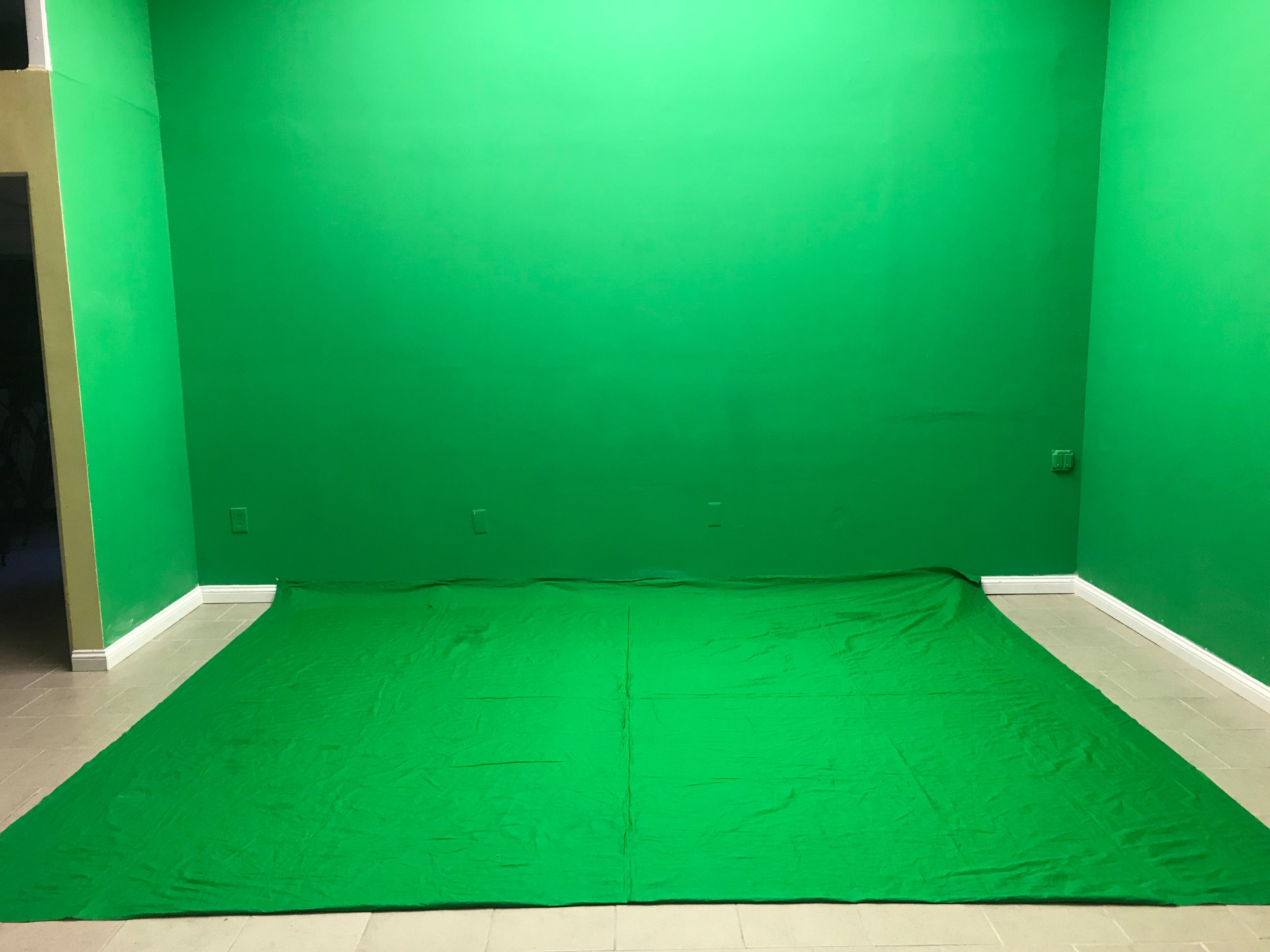 A room with a floor and wall covered in green fabric, creating a green screen setup.