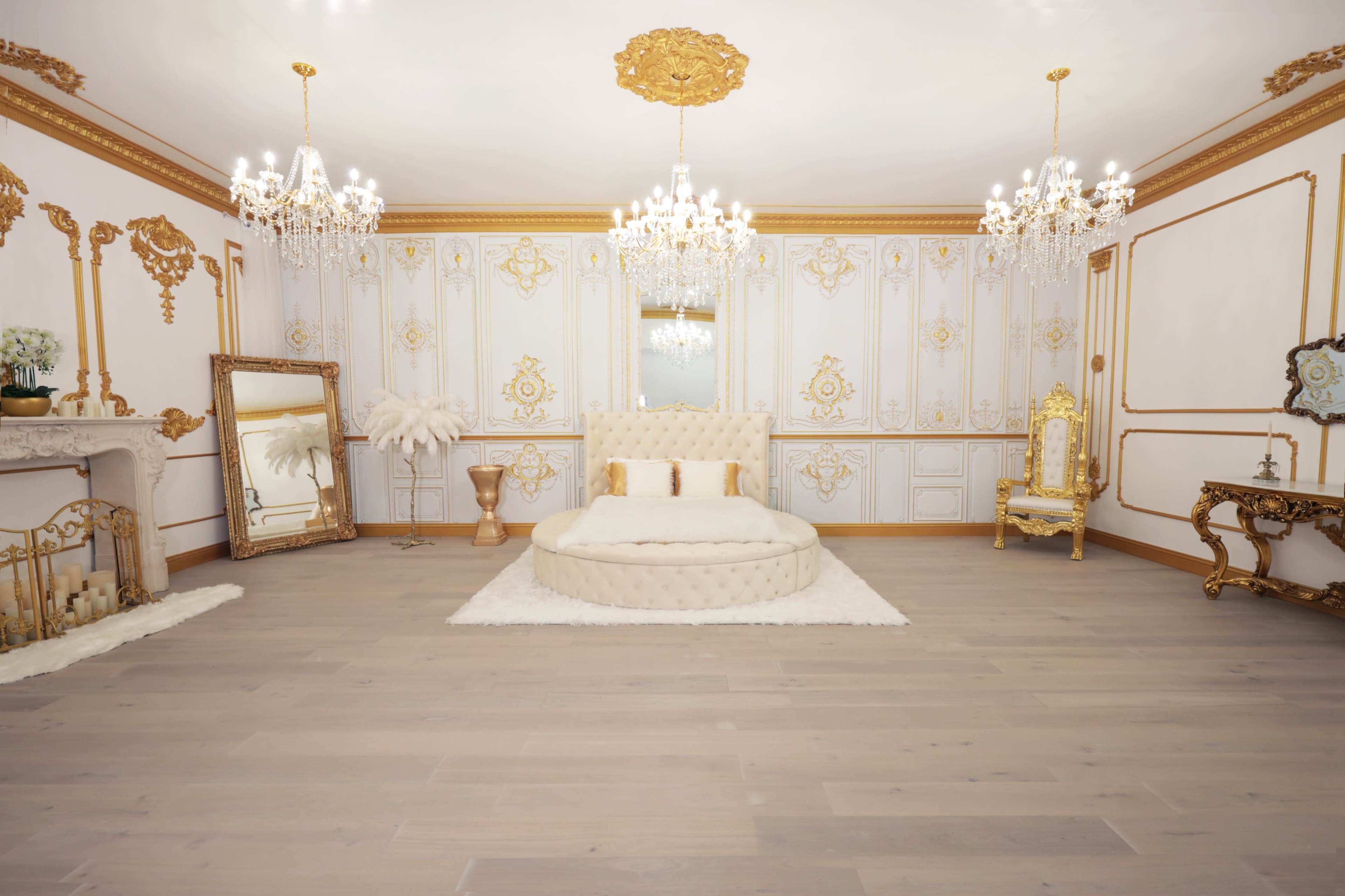 An opulent bedroom featuring a circular tufted bed, ornate chandeliers, and decorative wall panels with gold accents.