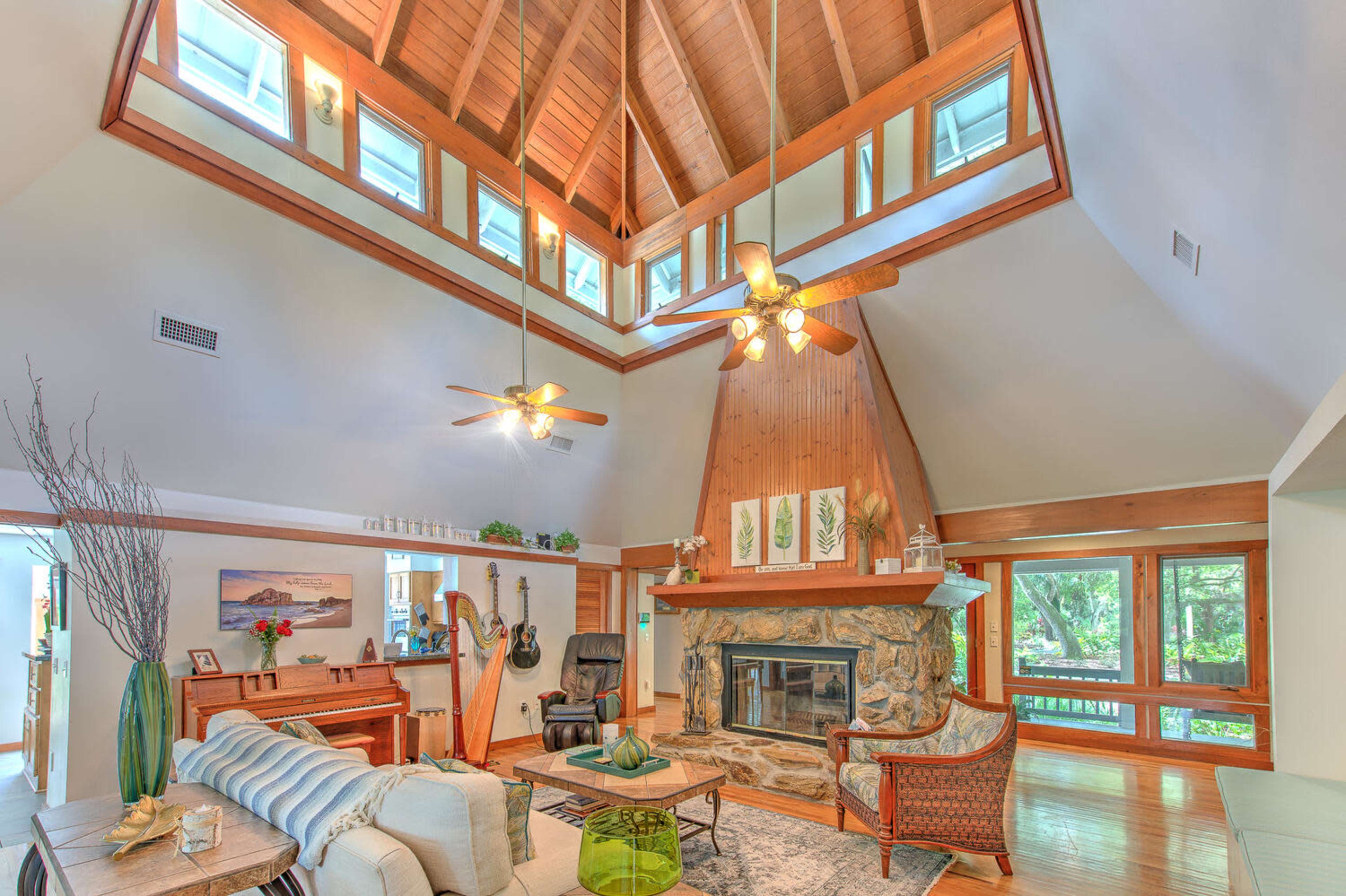 The living room features a high, wooden-beamed ceiling, a stone fireplace, and large windows overlooking a garden.