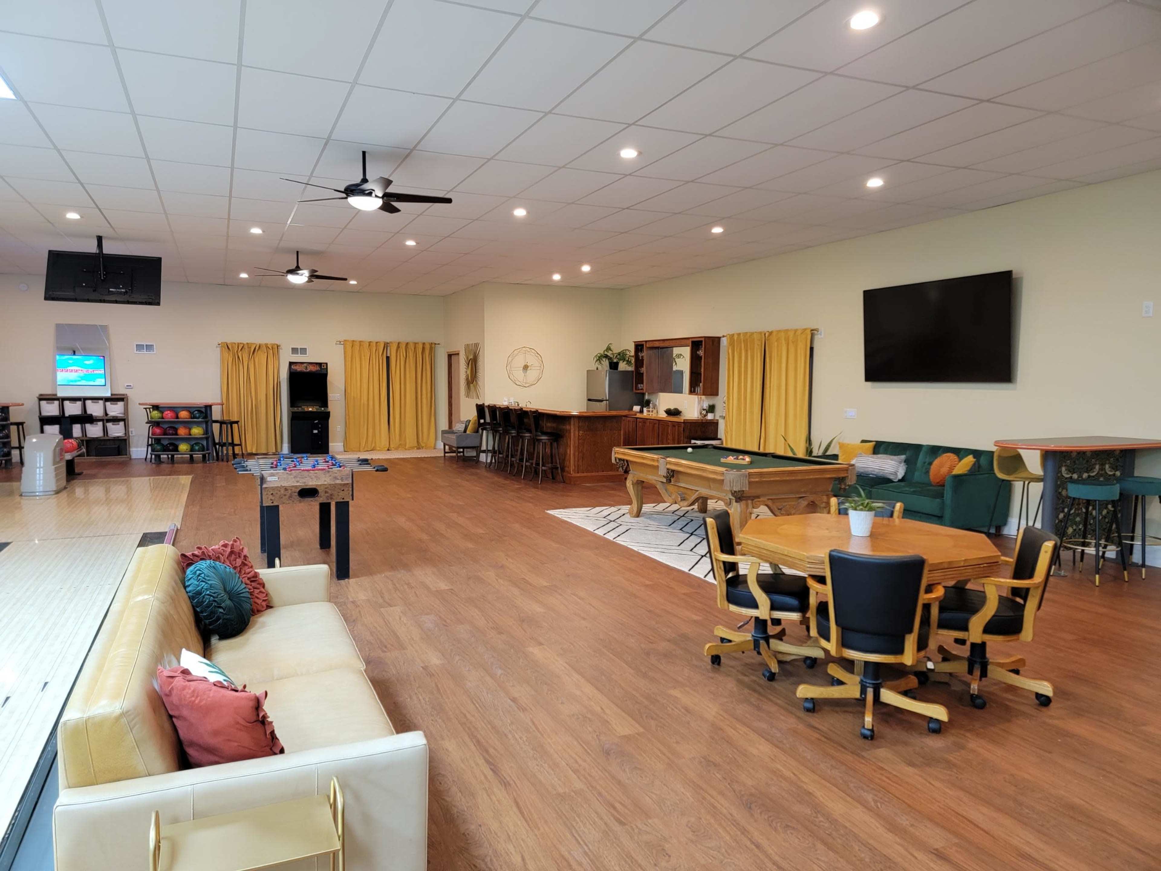 A spacious recreation room with various seating areas, a pool table, and a large television mounted on the wall.