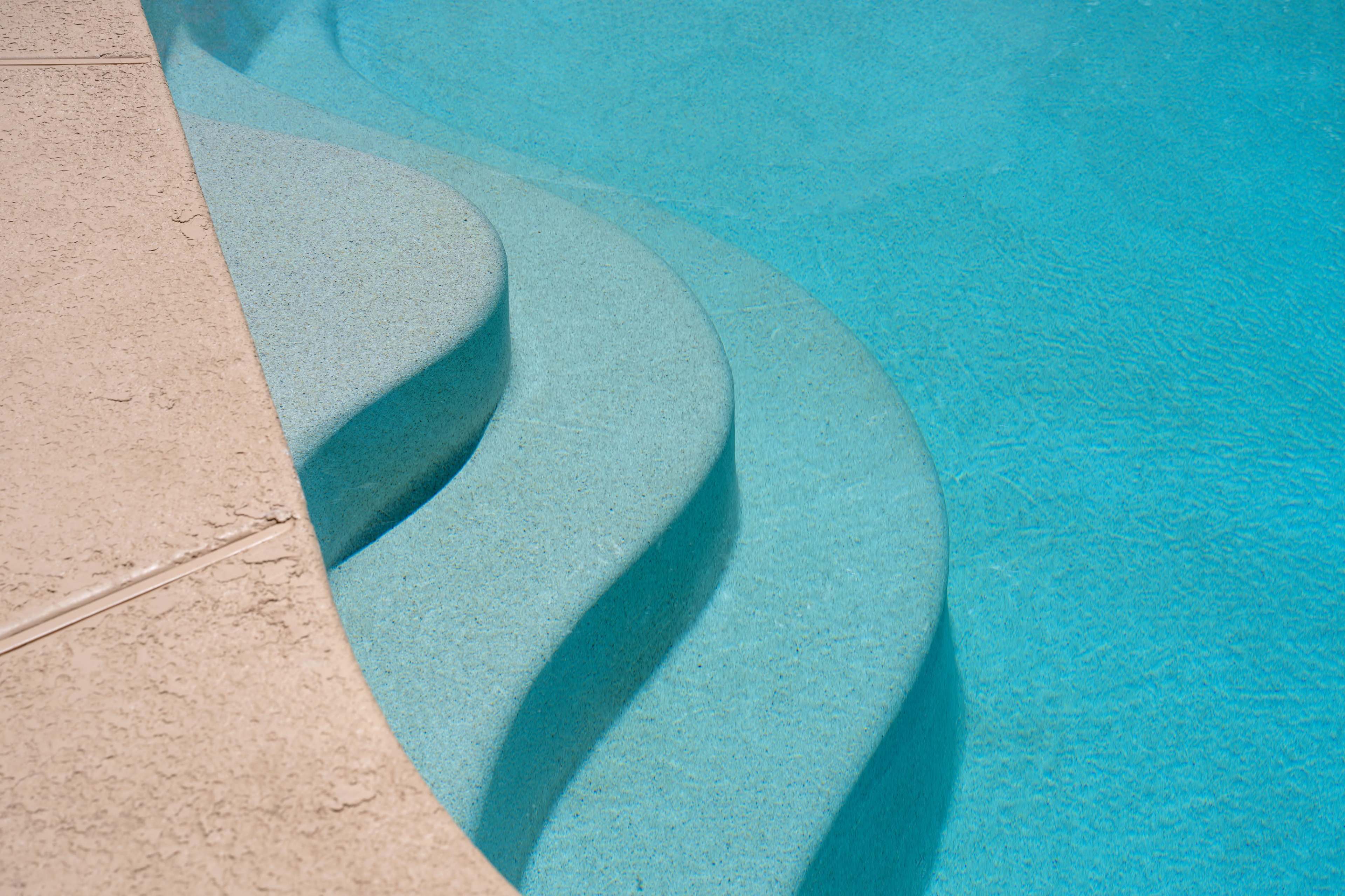 The image shows curved steps leading into a clear blue swimming pool.