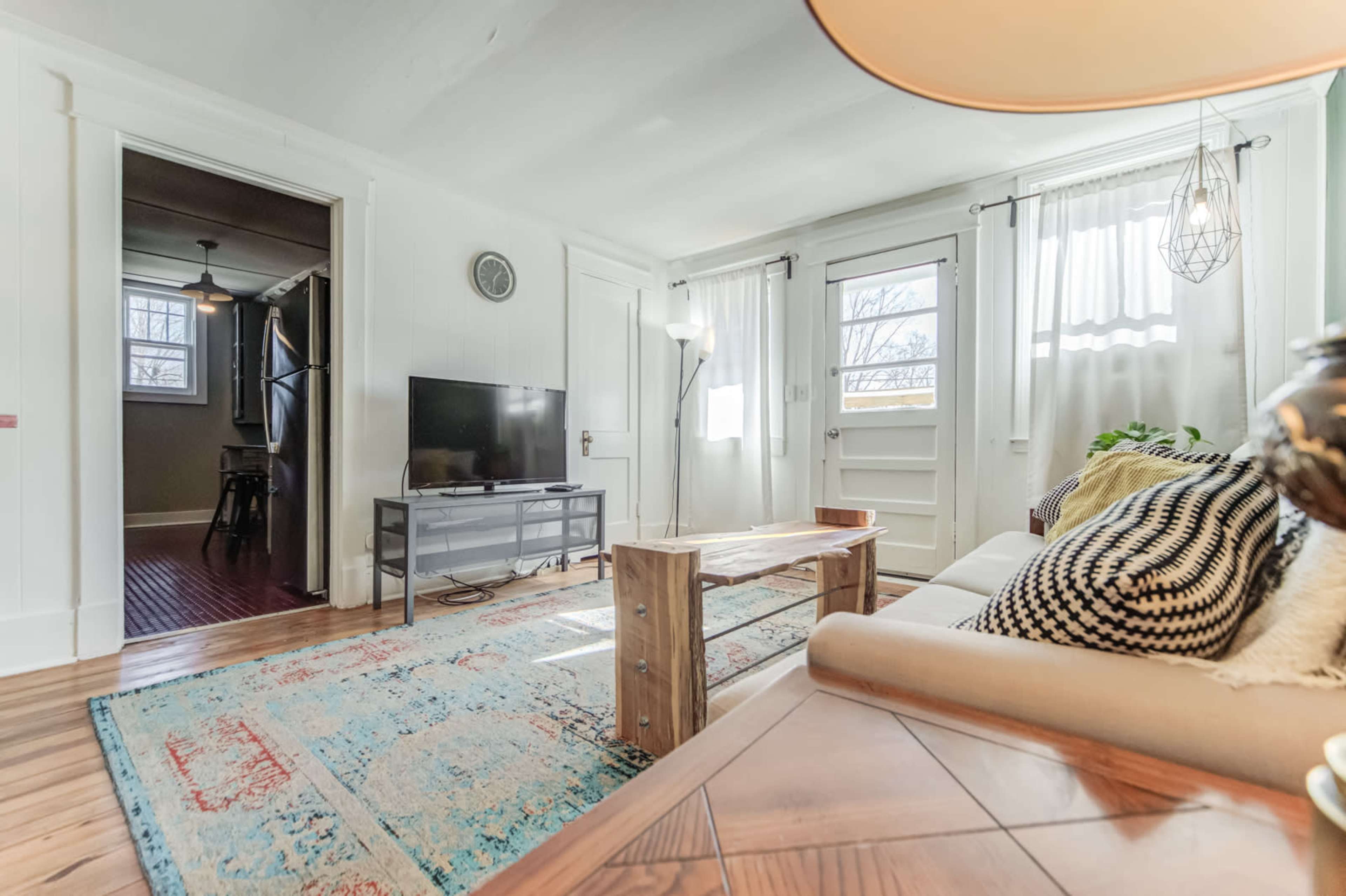 The living room features a couch, a wooden coffee table, a television on a stand, and large windows allowing natural light to enter.