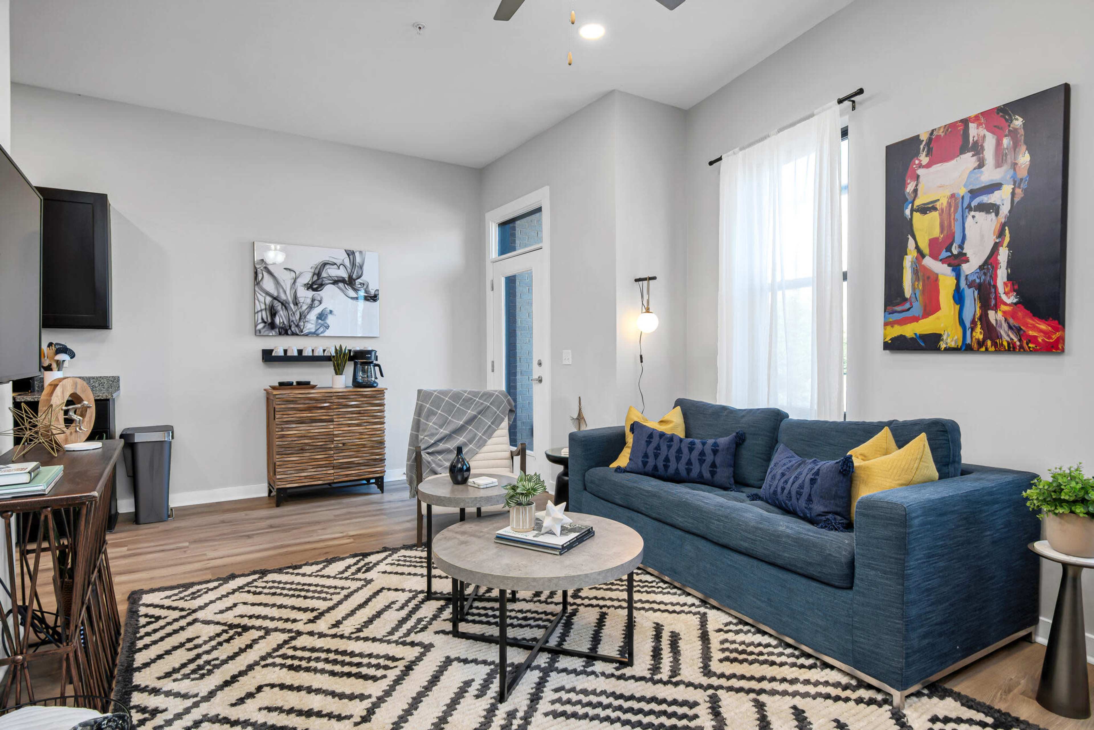 The living room features a blue sofa, a round coffee table, and an abstract painting on the wall, with a modern design and hardwood floors.