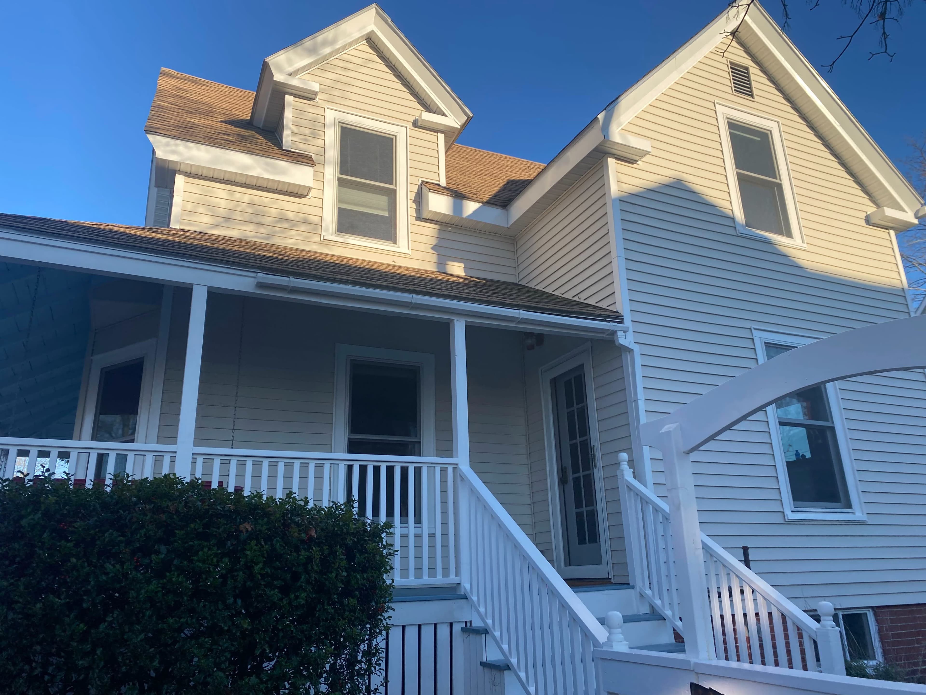 A two-story house with a gabled roof, a front porch, and white railings.