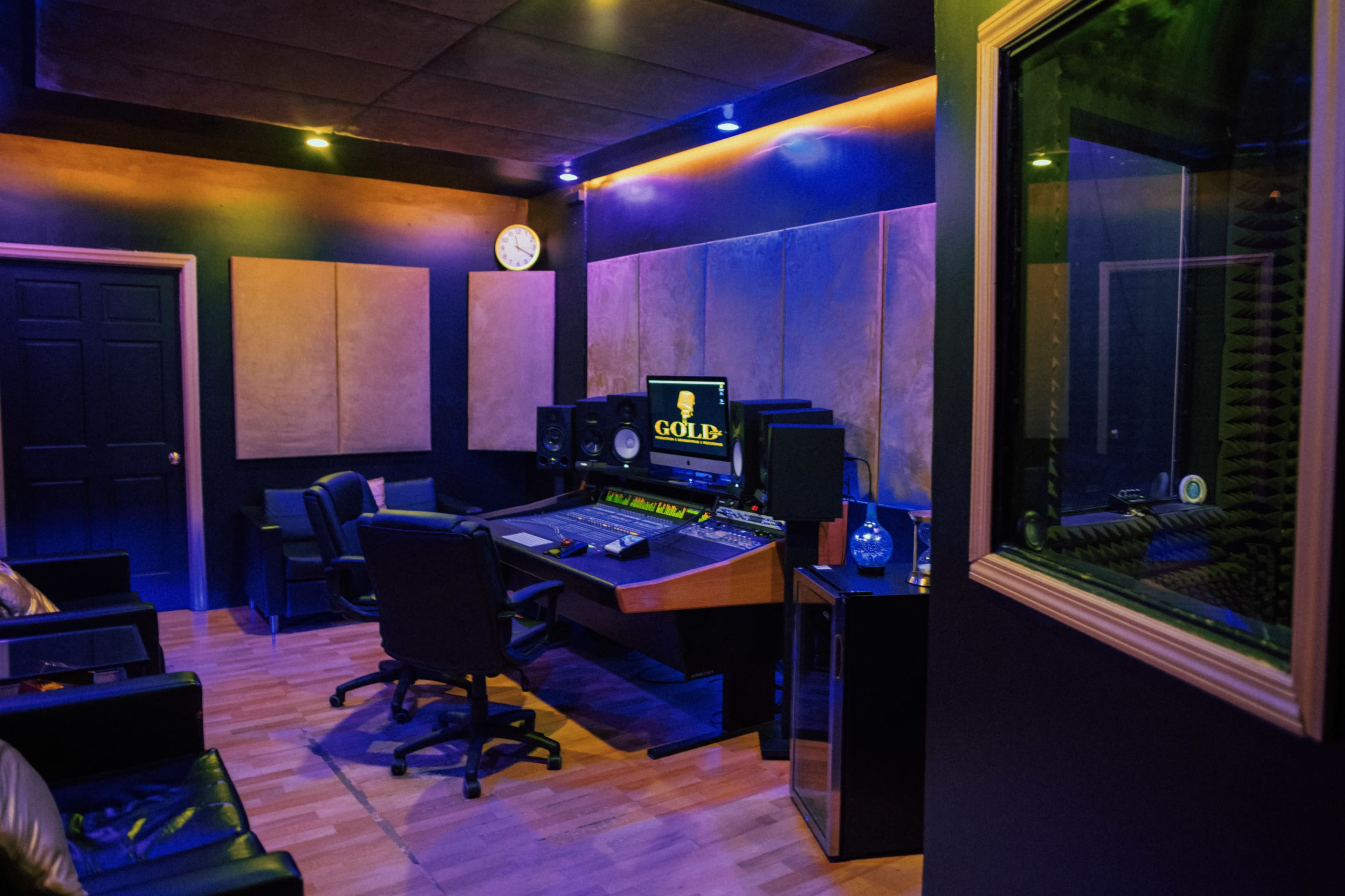 A music recording studio with a mixing console, speakers, and soundproofing panels, illuminated by ambient lighting.