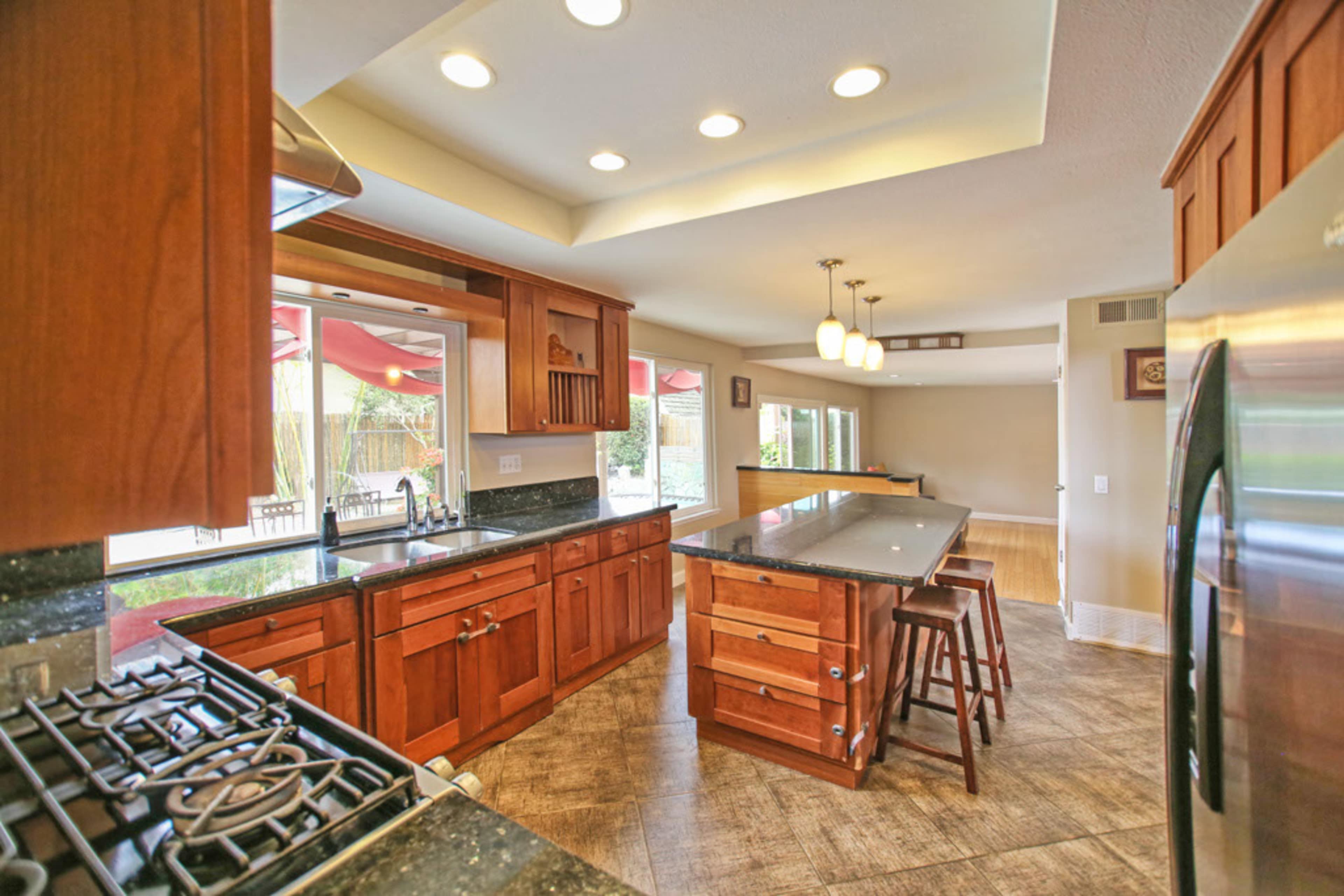 The image shows a modern kitchen with wooden cabinets, a granite countertop, and an island with seating.