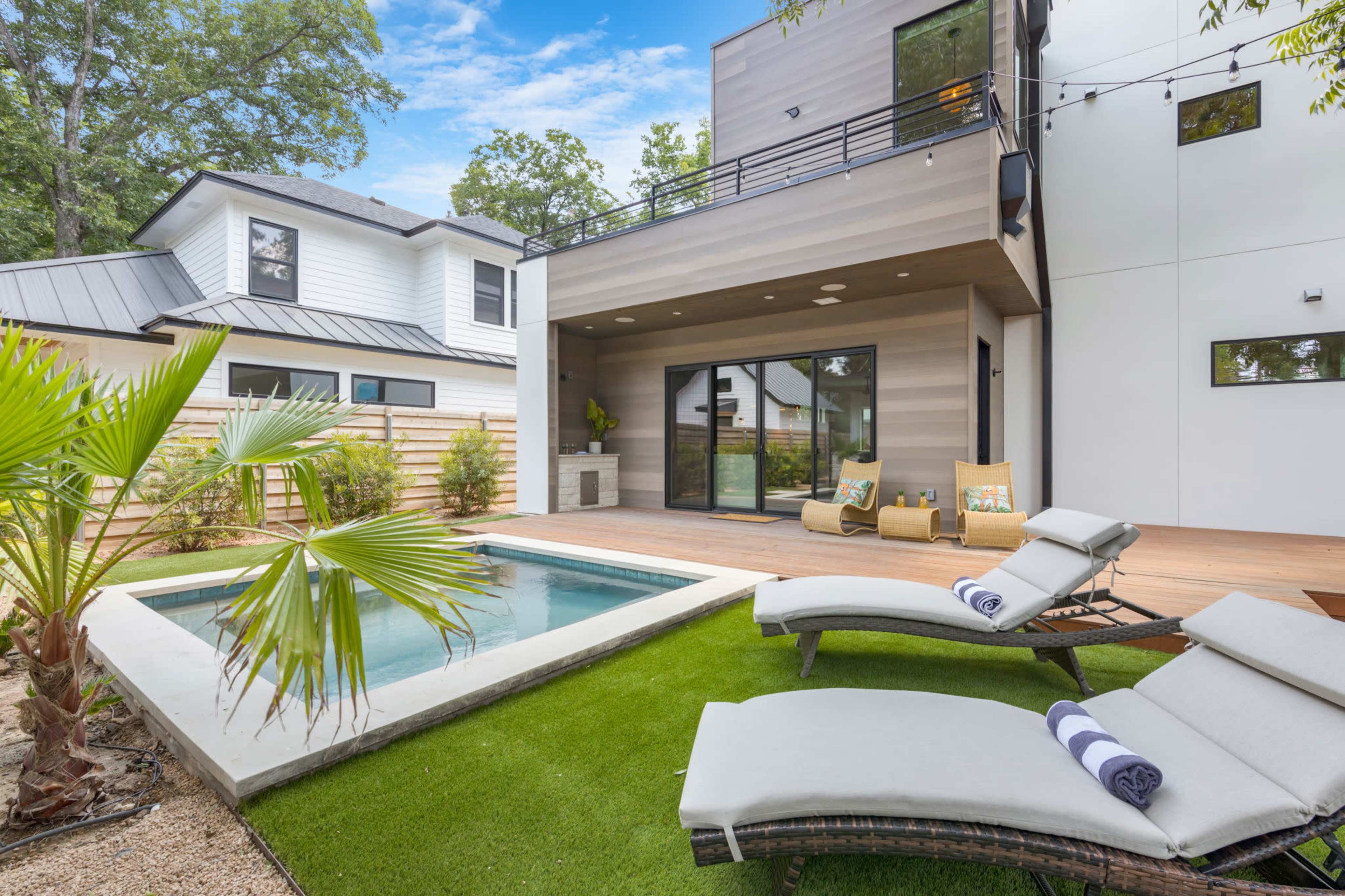 The image shows a modern outdoor area featuring a small pool, lounge chairs, and a landscaped patio surrounded by greenery.