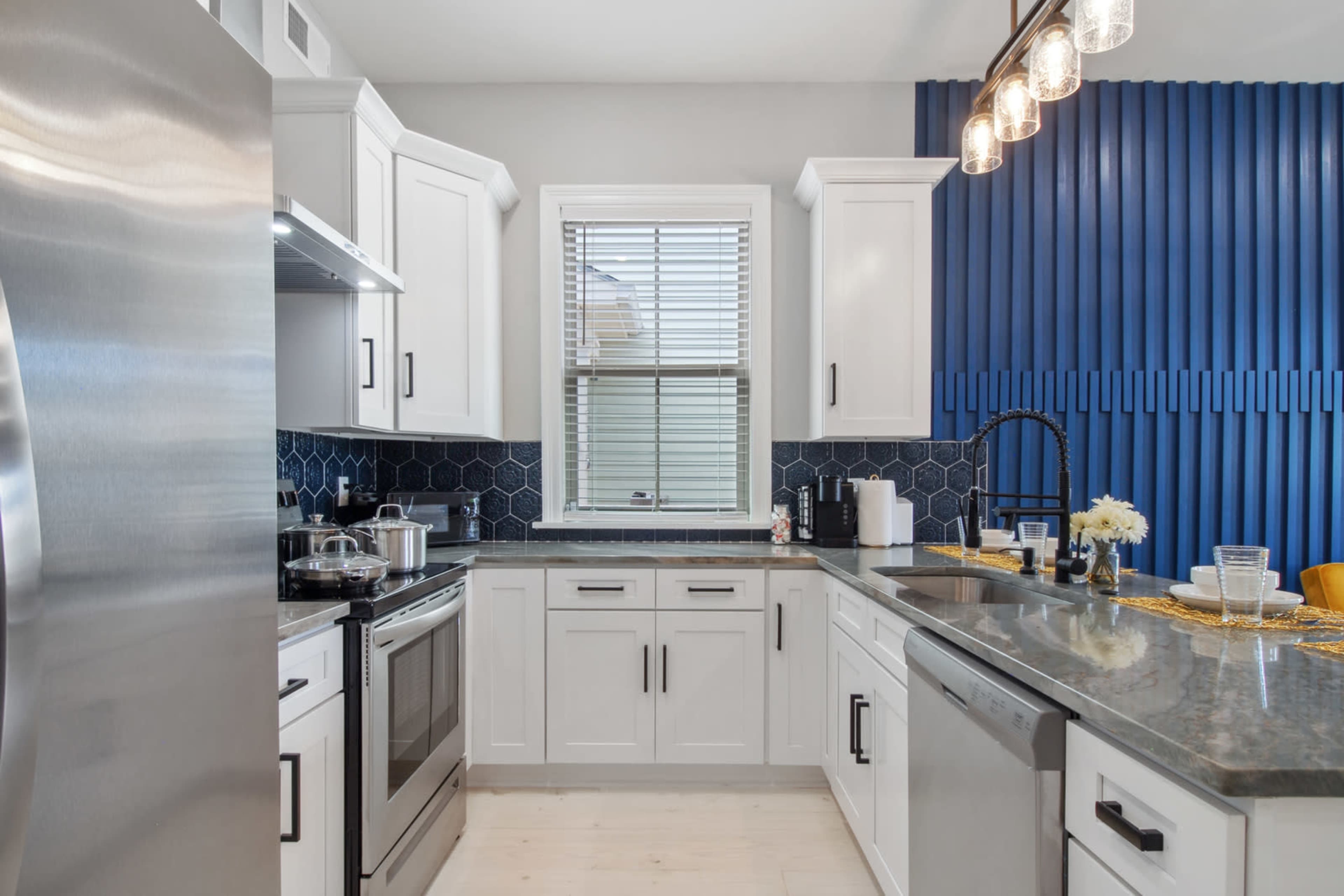 A compact kitchen features white cabinetry, stainless steel appliances, and a blue textured wall accent.