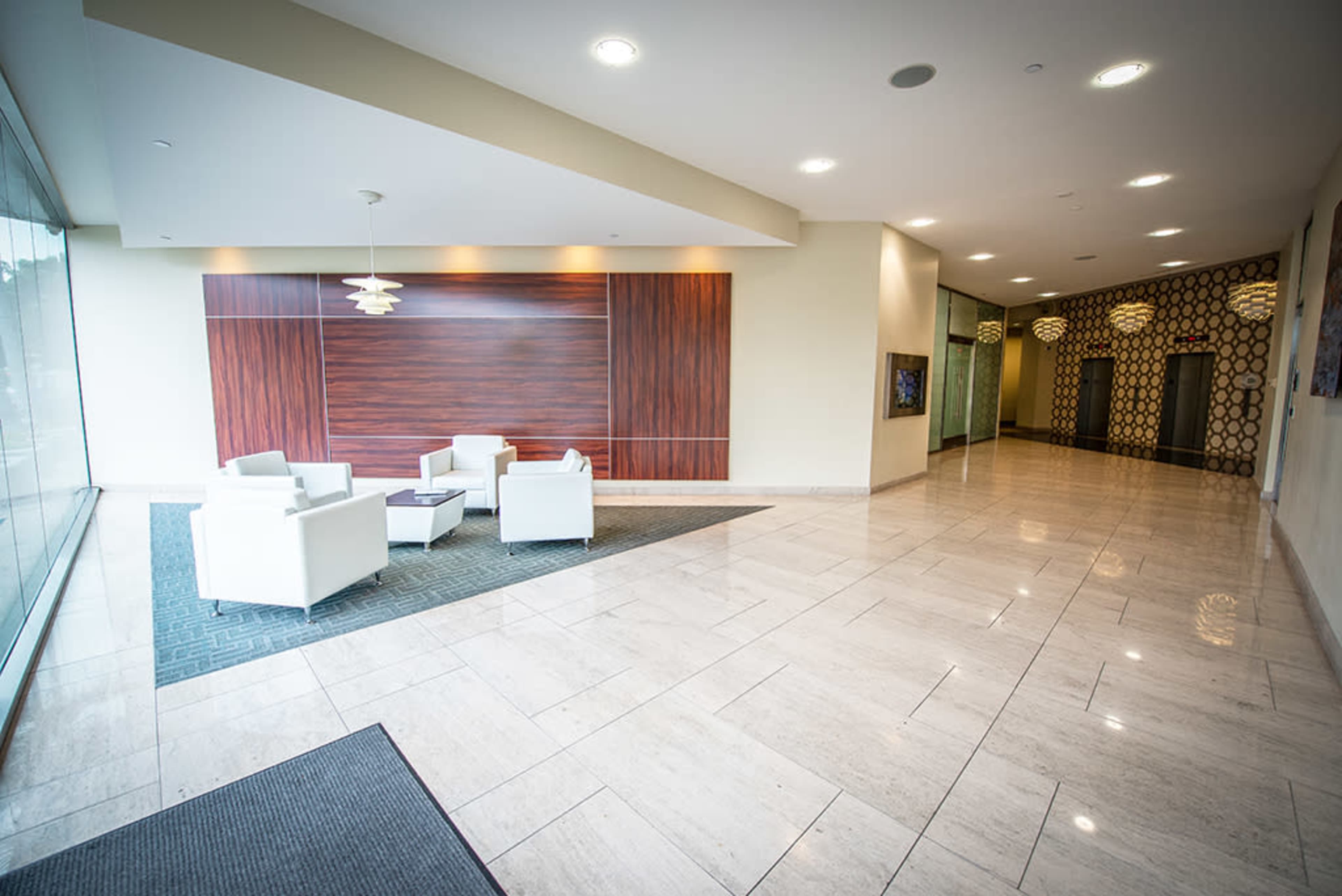 The image shows a modern lobby area with white armchairs arranged around a small table, against a backdrop of wooden paneling and sleek walls.