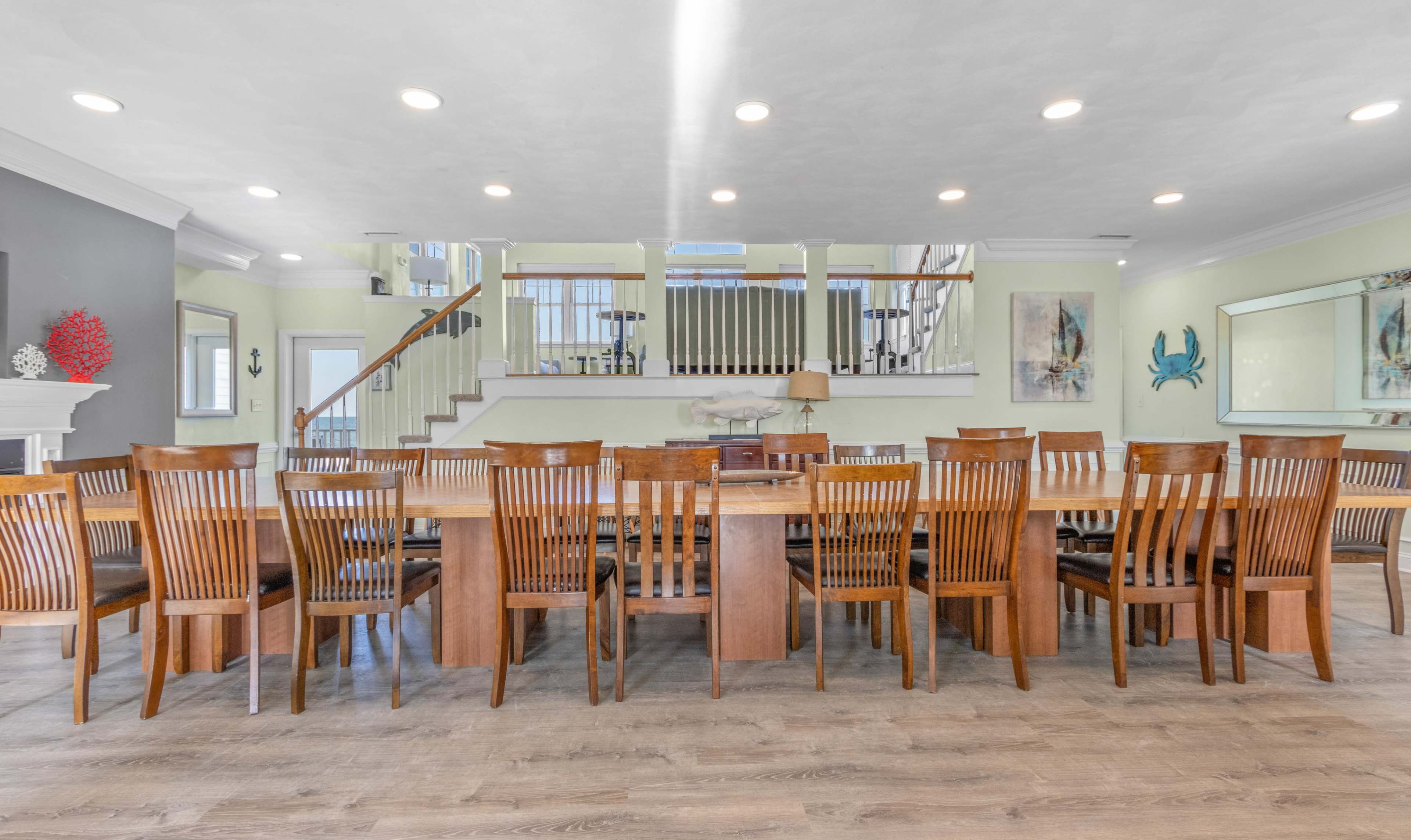 A spacious dining room features a large wooden table surrounded by multiple chairs, with a staircase visible in the background.