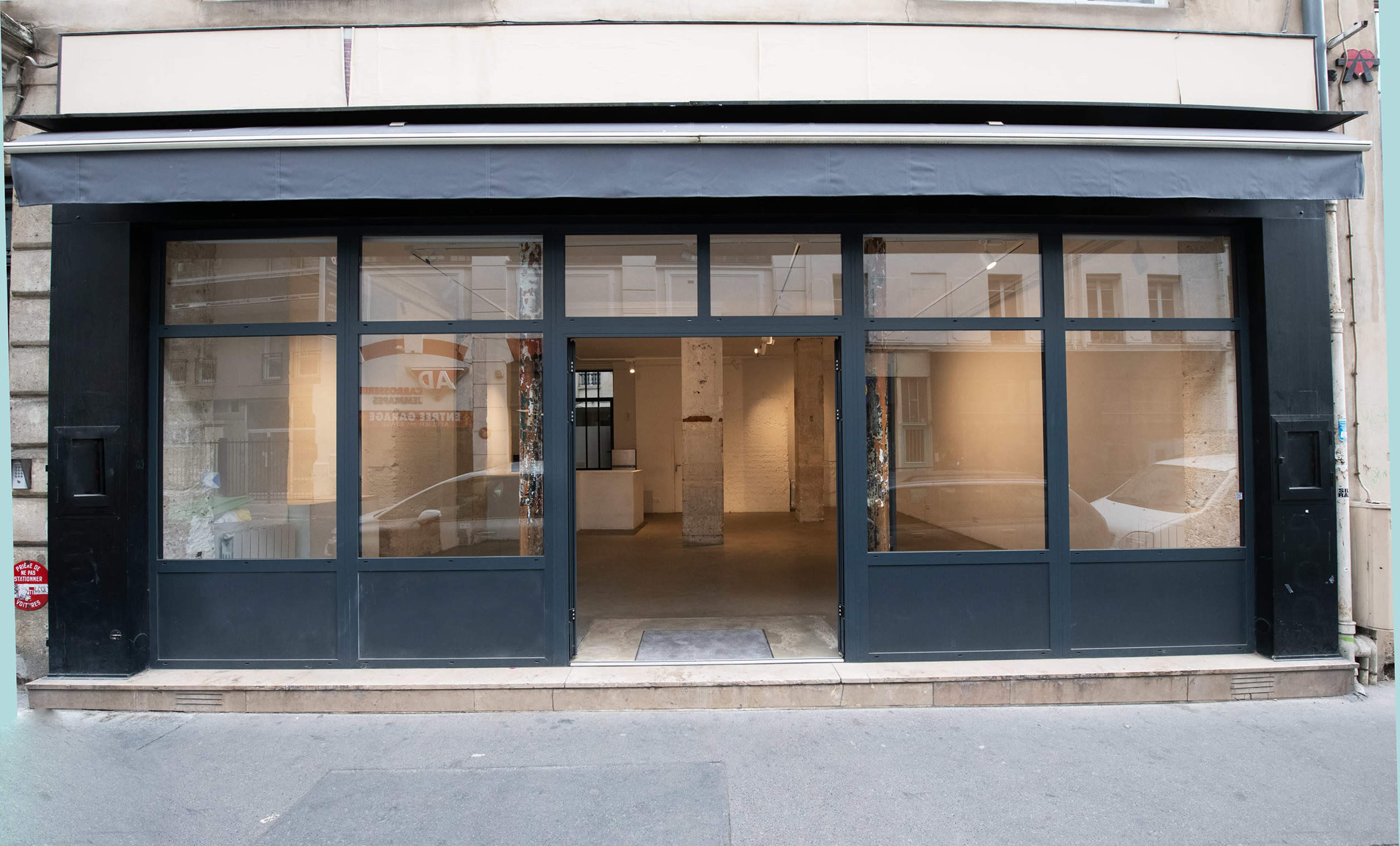 The image shows the exterior of a storefront with large glass windows and an awning, located on a street.