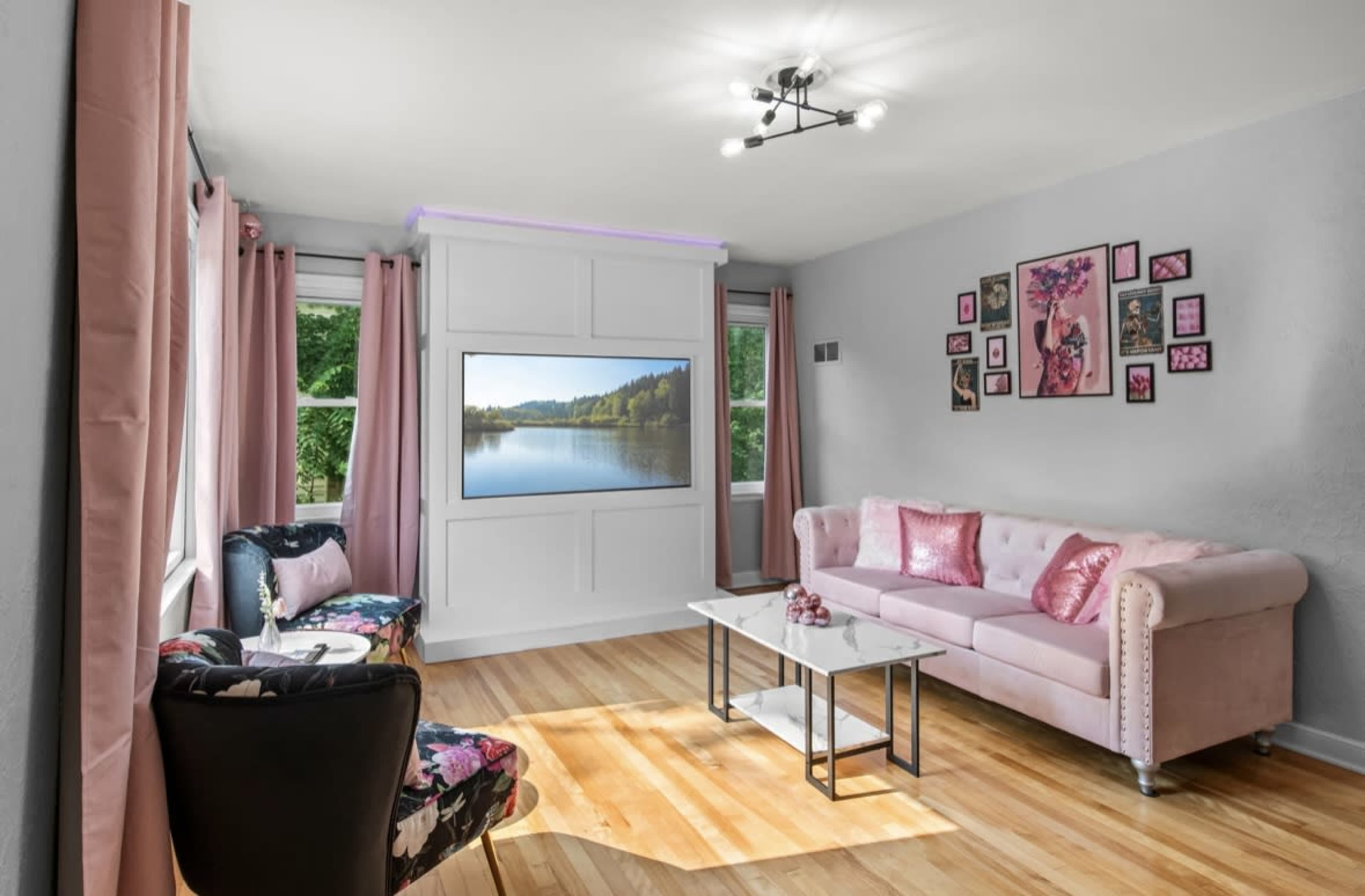 The living room features a pink sofa, a black and floral accent chair, a coffee table, and a wall-mounted television with a view of a lake.