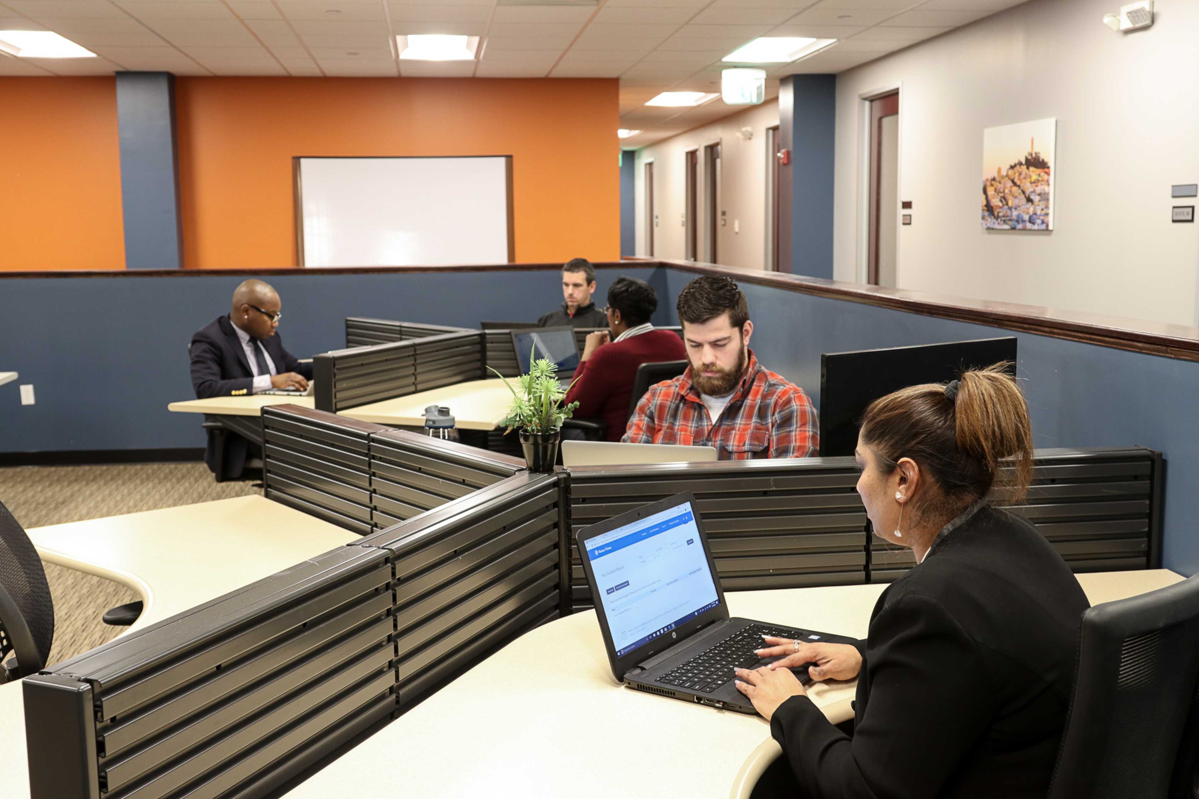 A shared office space with four individuals working on laptops at separate desks.