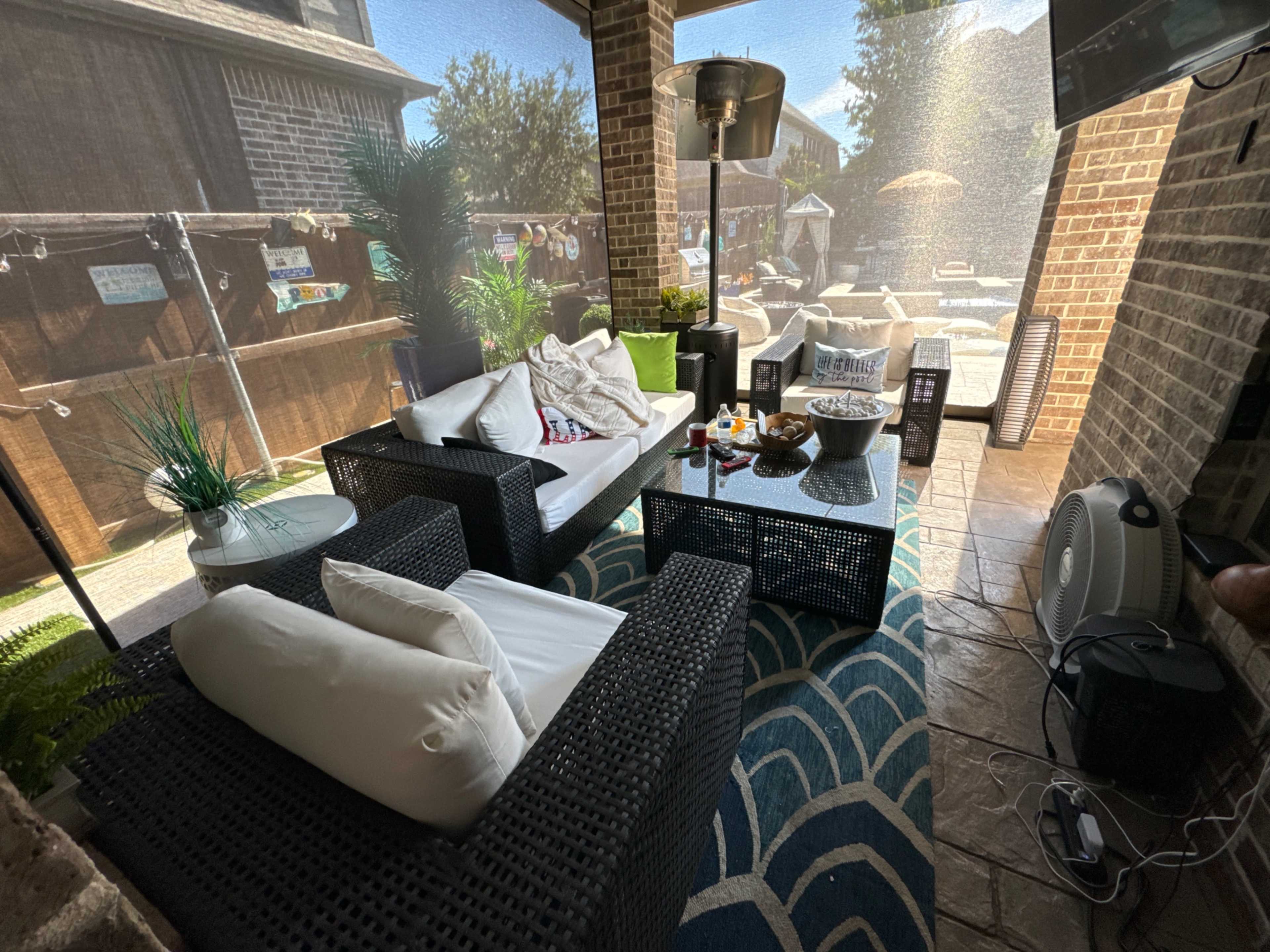 The image shows a screened patio furnished with black wicker seating, a coffee table with snacks, and a view of an outdoor pool area.