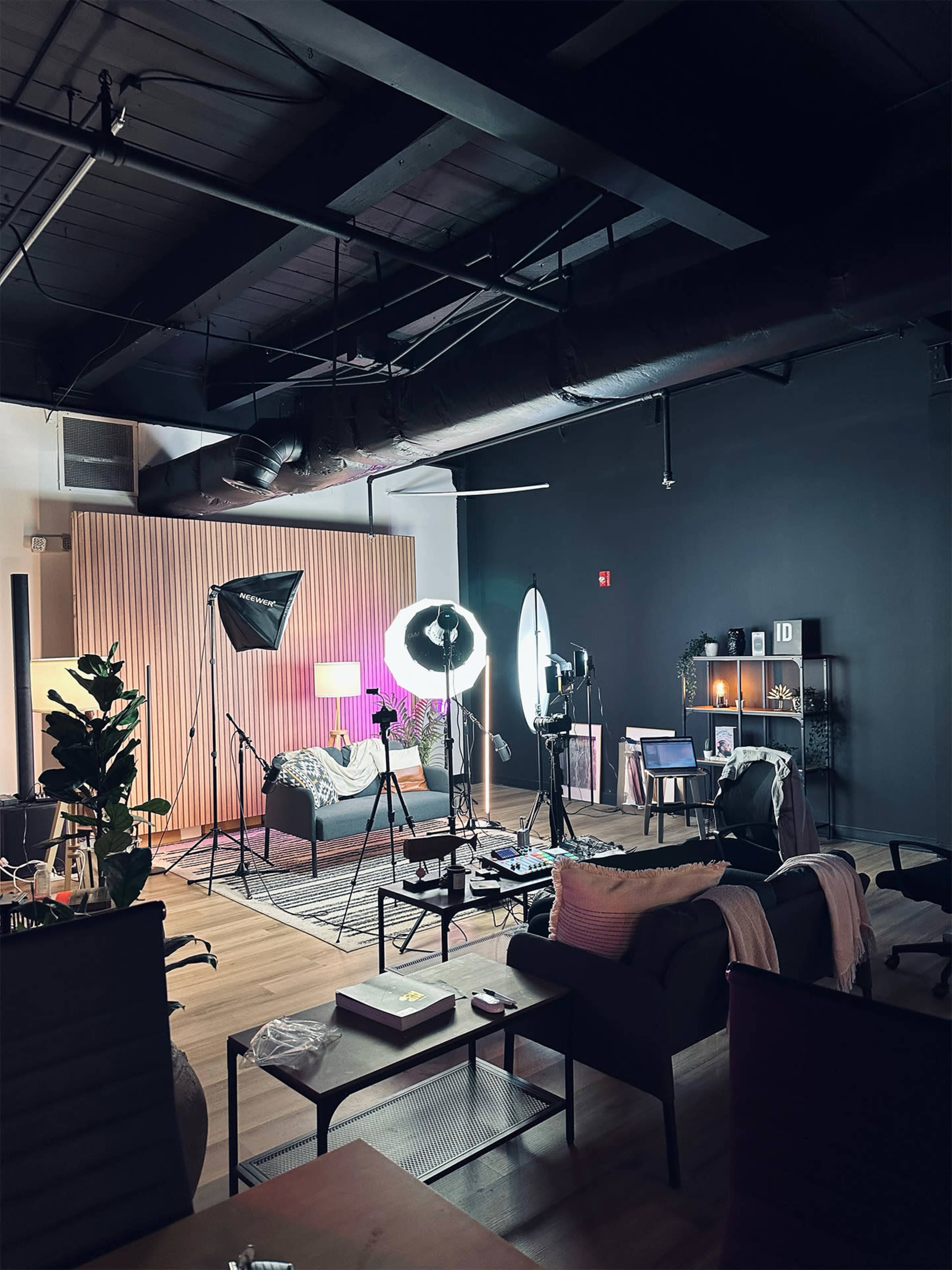 A well-lit studio setup with various photography equipment, including softboxes and reflectors, in a modern living space featuring a couch and decorative plants.