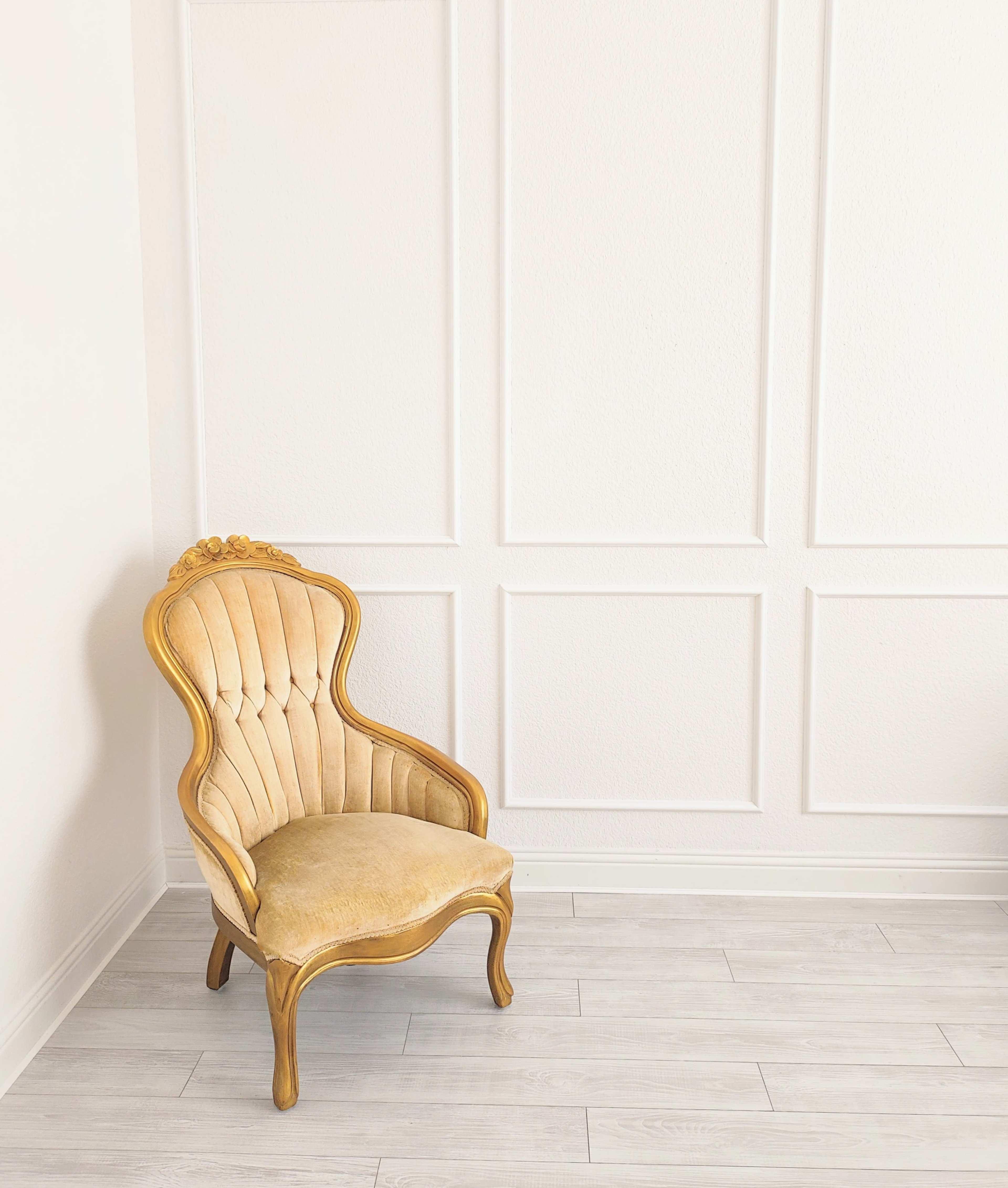 A vintage gold-accented armchair sits against a plain white wall in a bright room.