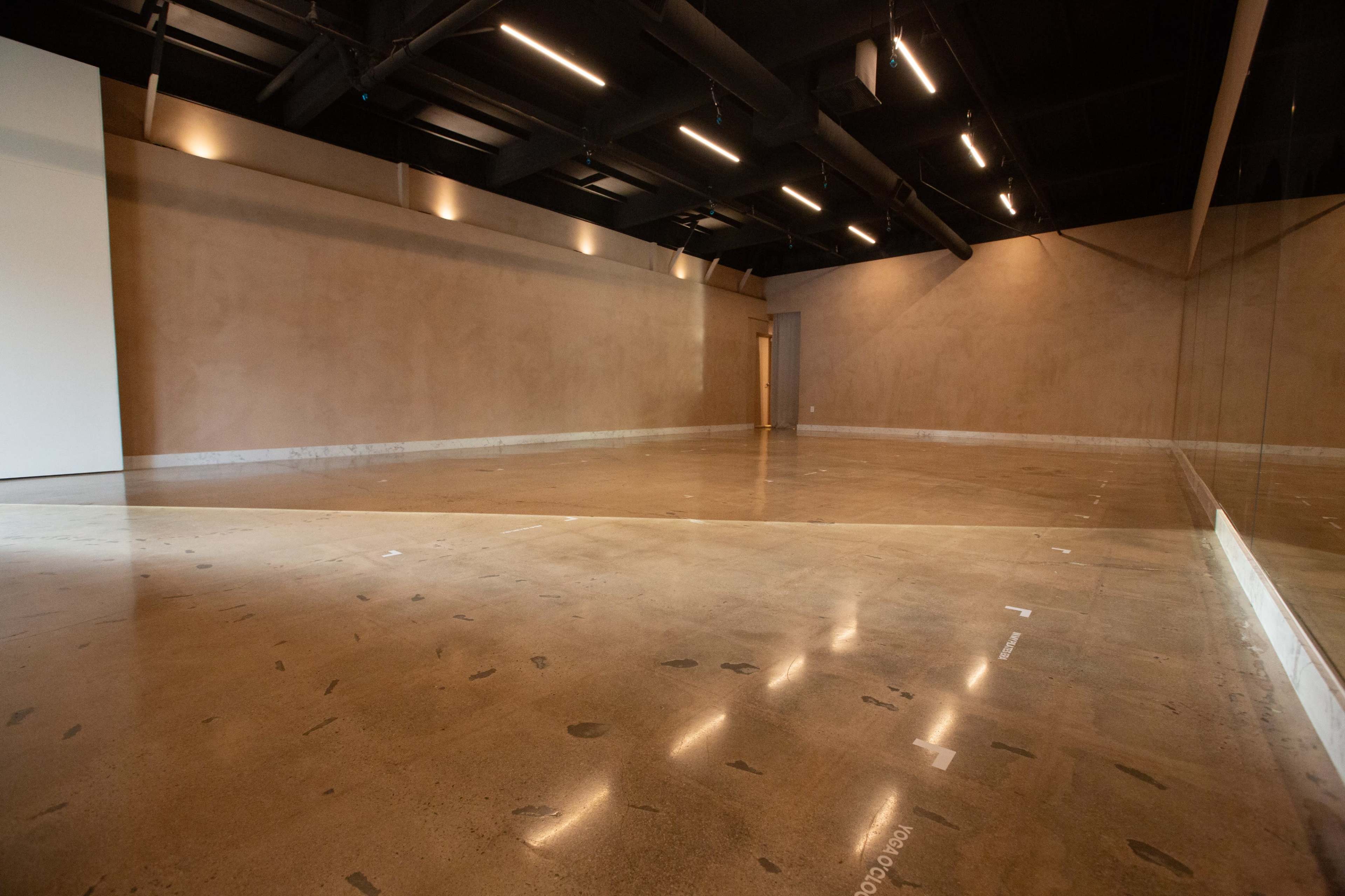 The image shows an empty studio space with a smooth, polished concrete floor and a large mirror on one wall.