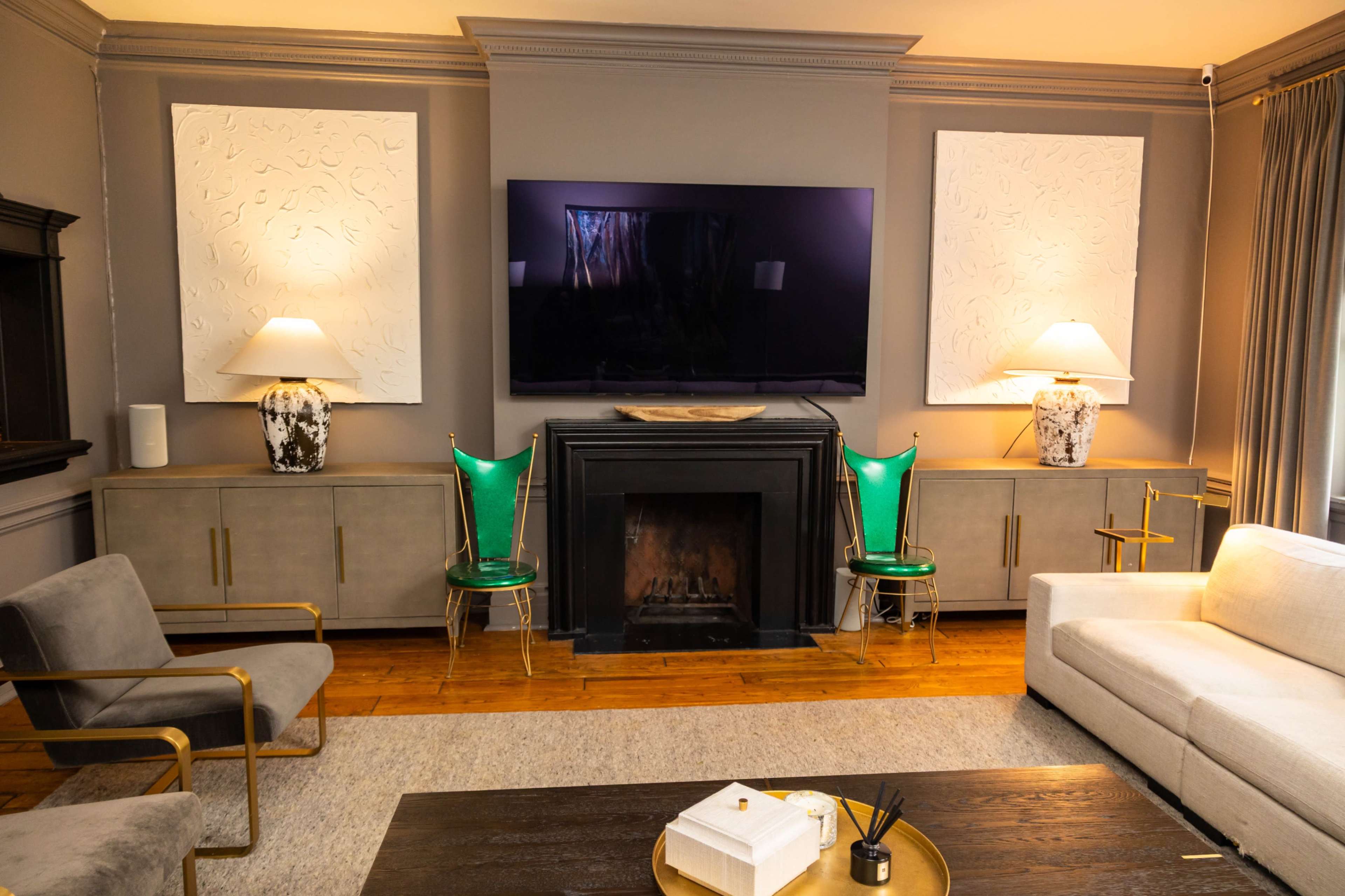 The image shows a modern living room with a fireplace, a large television mounted on the wall, two lamps on either side, and seating arranged around a coffee table.