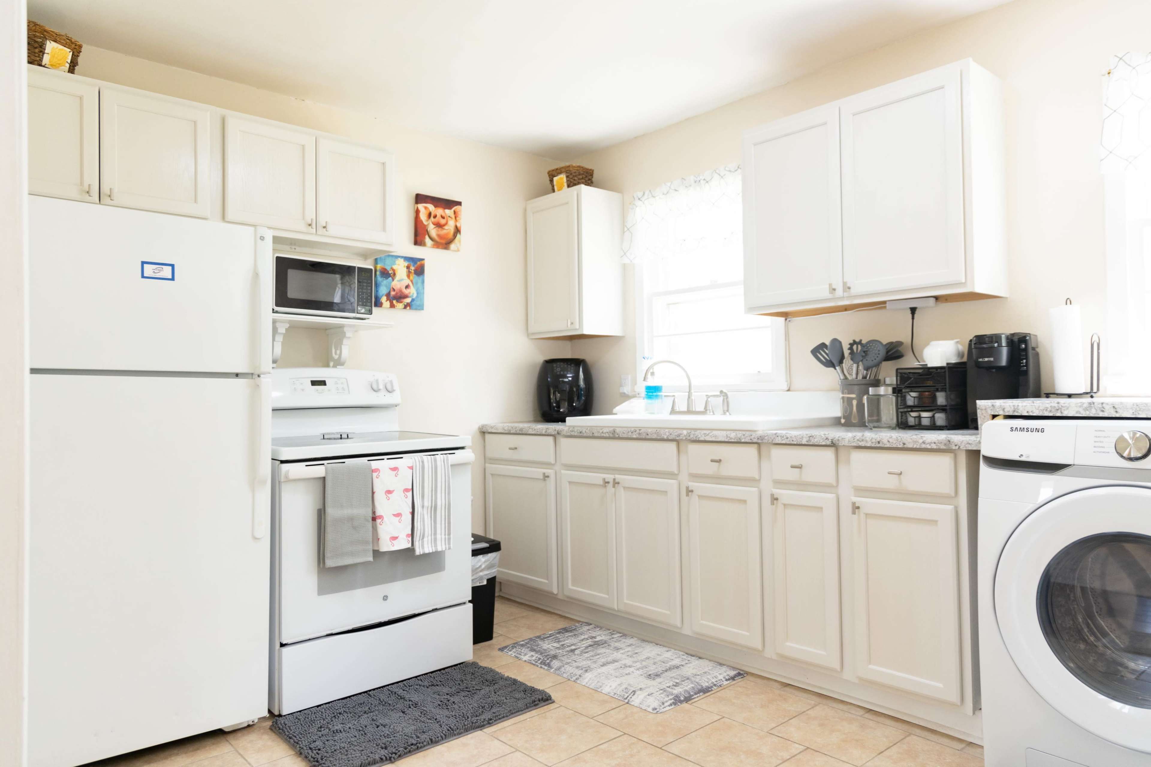 A modern kitchen with white cabinets, a refrigerator, and a stove, featuring a sink and various kitchen appliances on the counter.