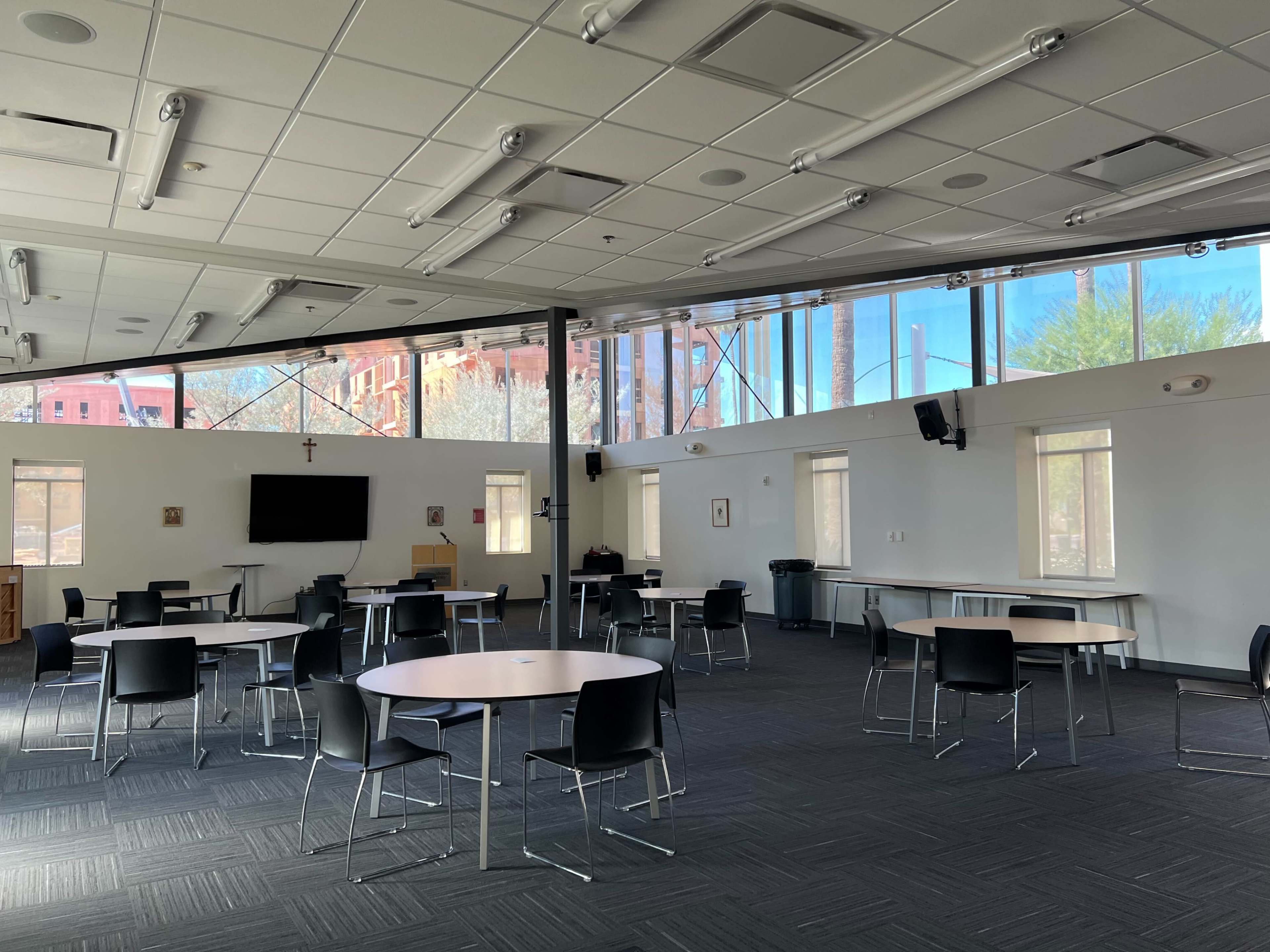 A spacious, well-lit room with several round tables and chairs arranged for meetings, featuring large windows that overlook a construction site.