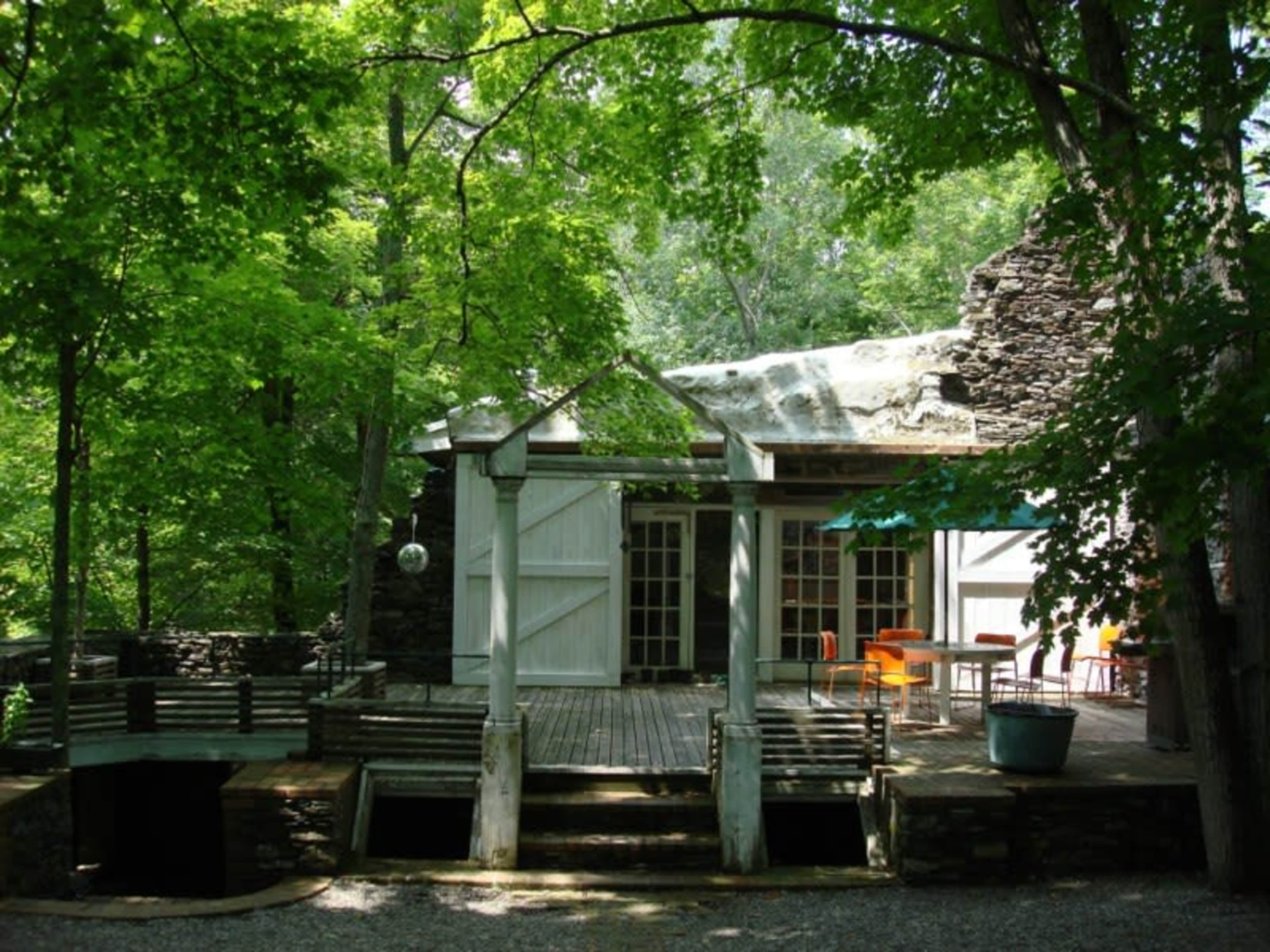 A modern cabin is situated in a wooded area, featuring large glass doors that open onto a wooden deck surrounded by trees.